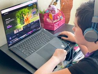 A teen sitting at a desk with headphones on, looking at the Amazon Prime Gaming home page on a laptop.