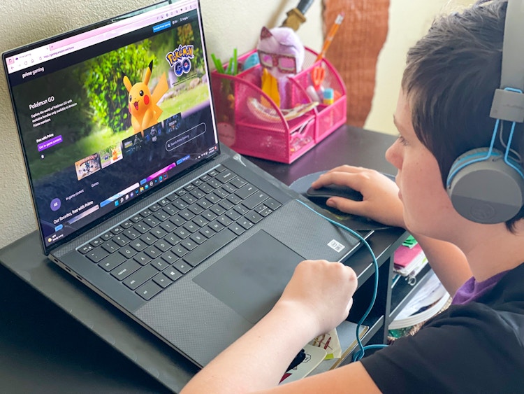 A teen sitting at a desk with headphones on, looking at the Amazon Prime Gaming home page on a laptop.