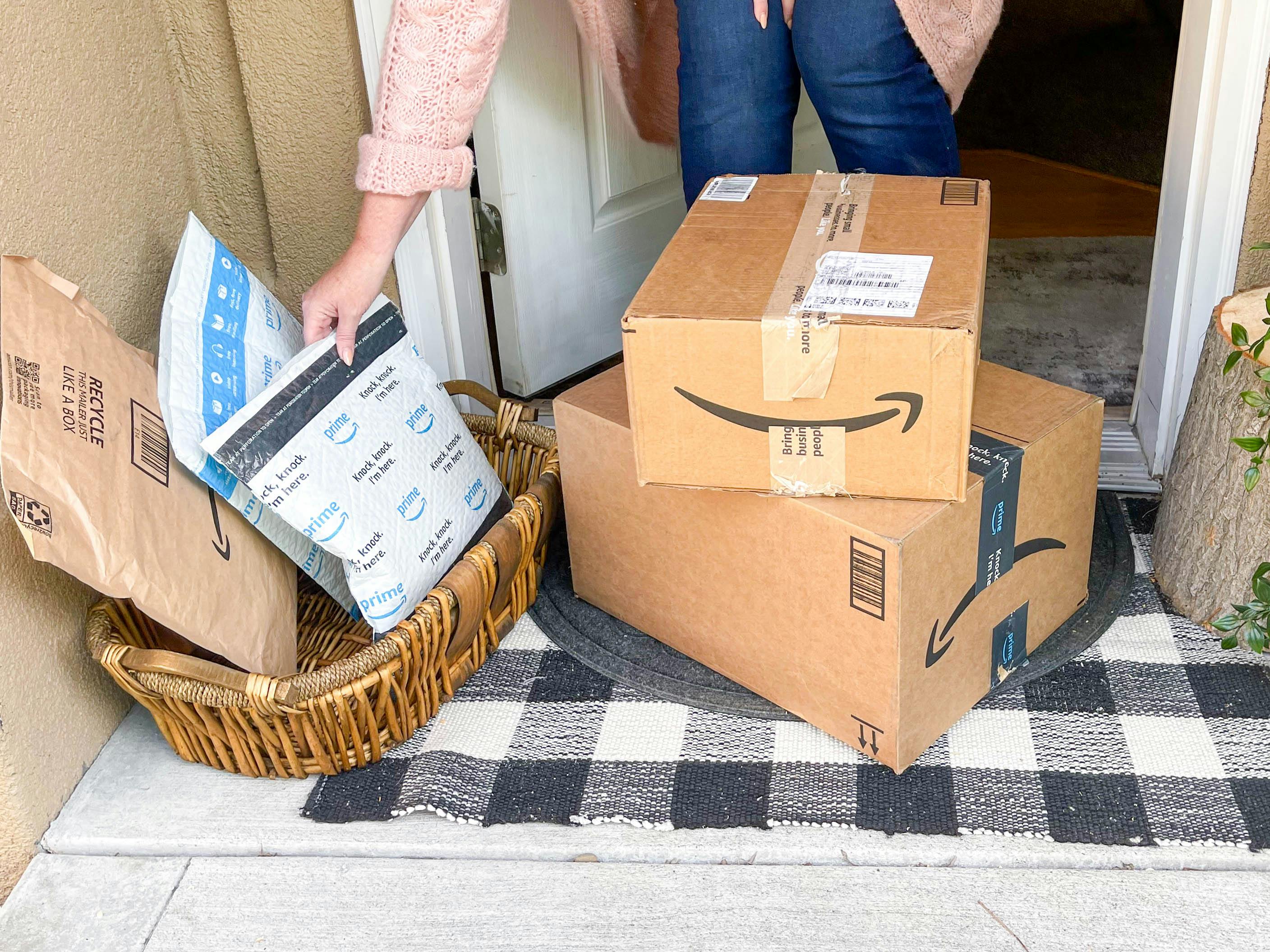 a person picking up an amazon package from a basket with packages and boxes on front porch
