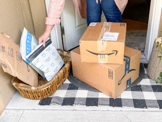 a person picking up an amazon package from a basket with packages and boxes on front porch