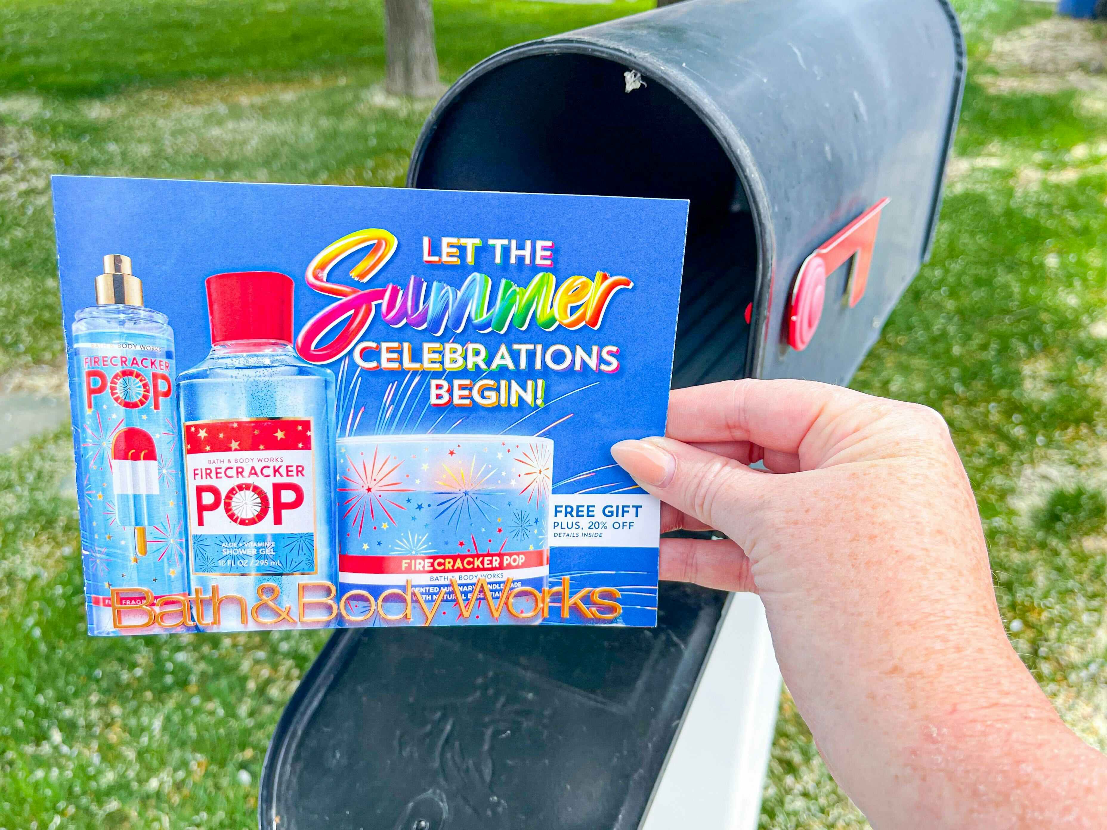 A person's hand taking a Bath & Body Works coupon mailer out of their mailbox.