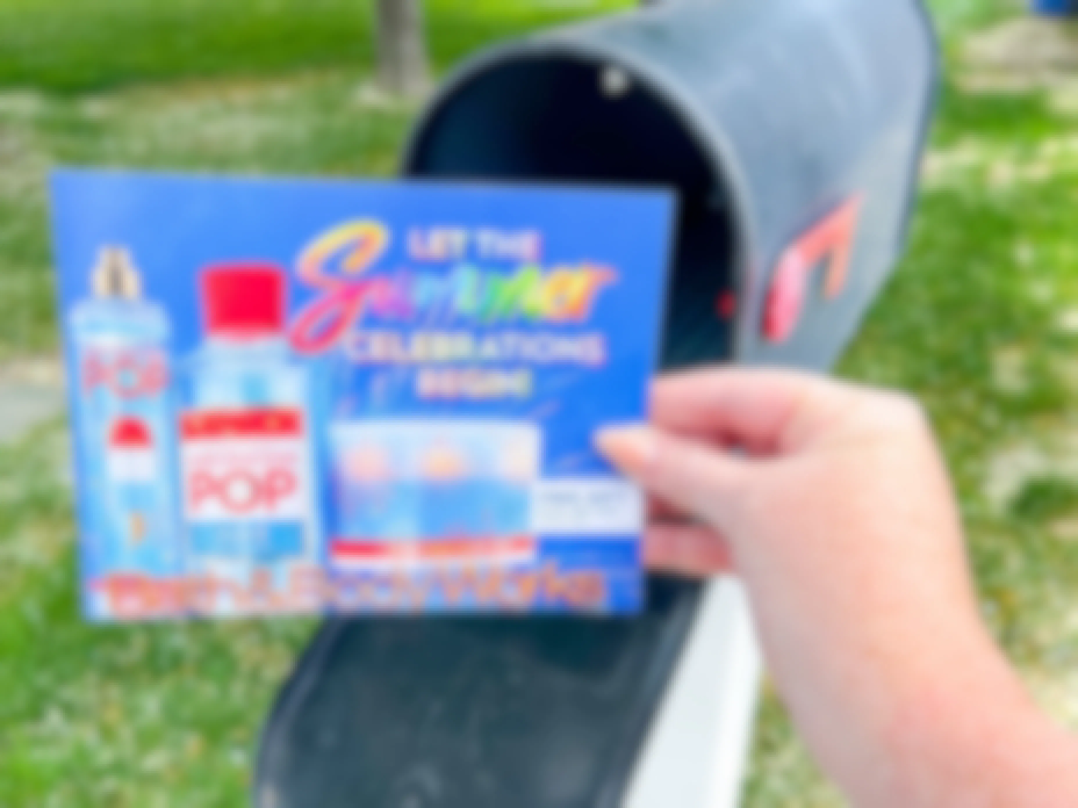 A person's hand taking a Bath & Body Works coupon mailer out of their mailbox.