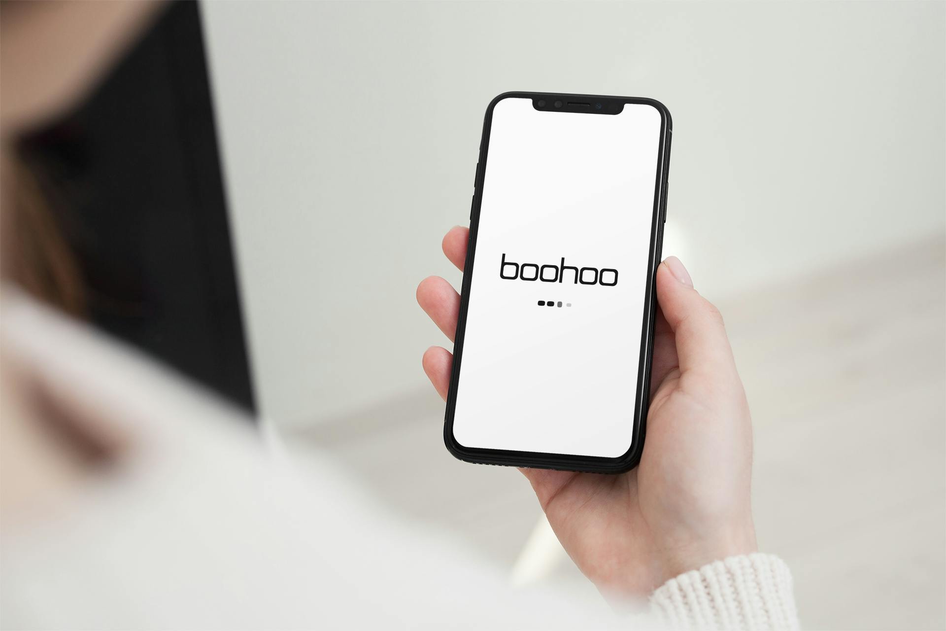 A person holding an iPhone displaying the boohoo app start up screen.