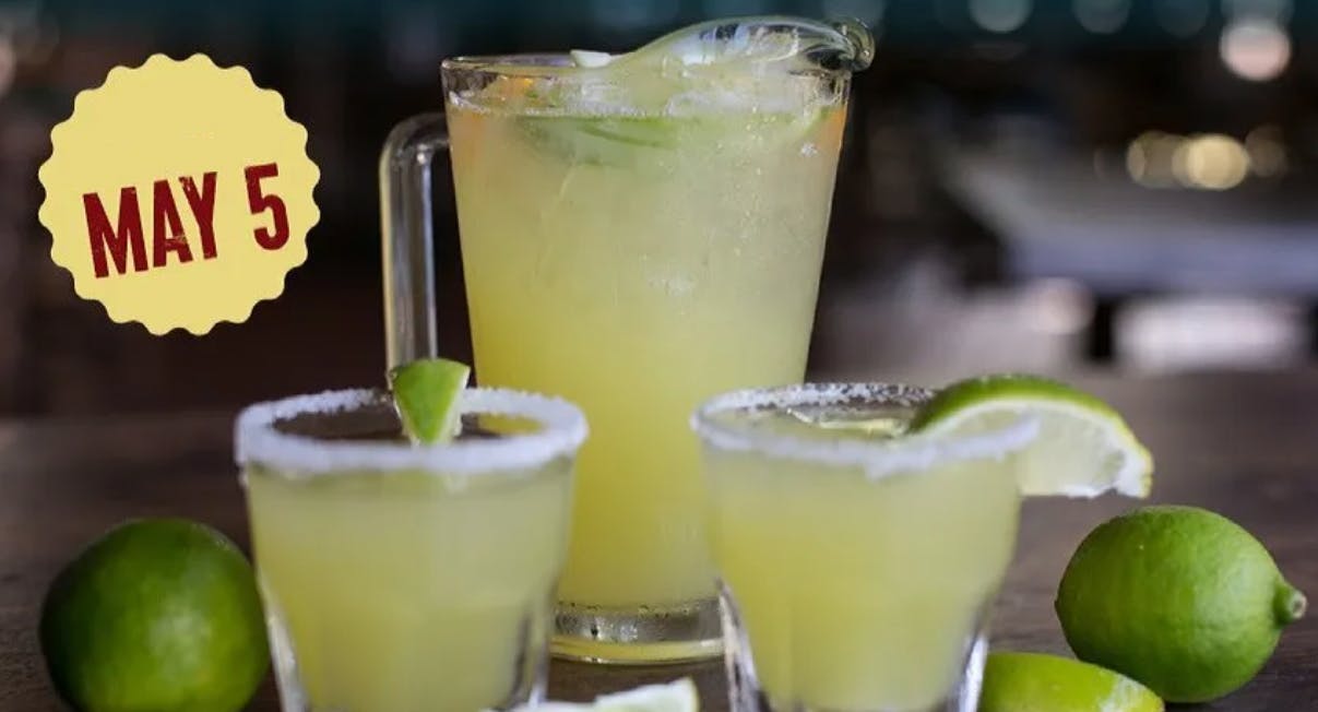 A margarita pitcher with two salt-rimmed glasses next to some limes with a graphic that says "May 5