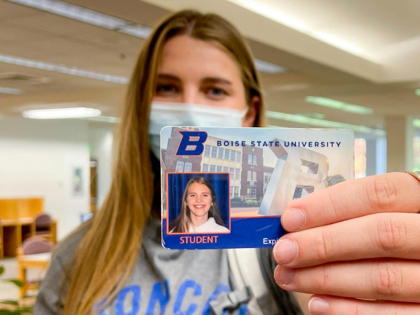 A student wearing a mask, holding up her ID card for Boise State University.