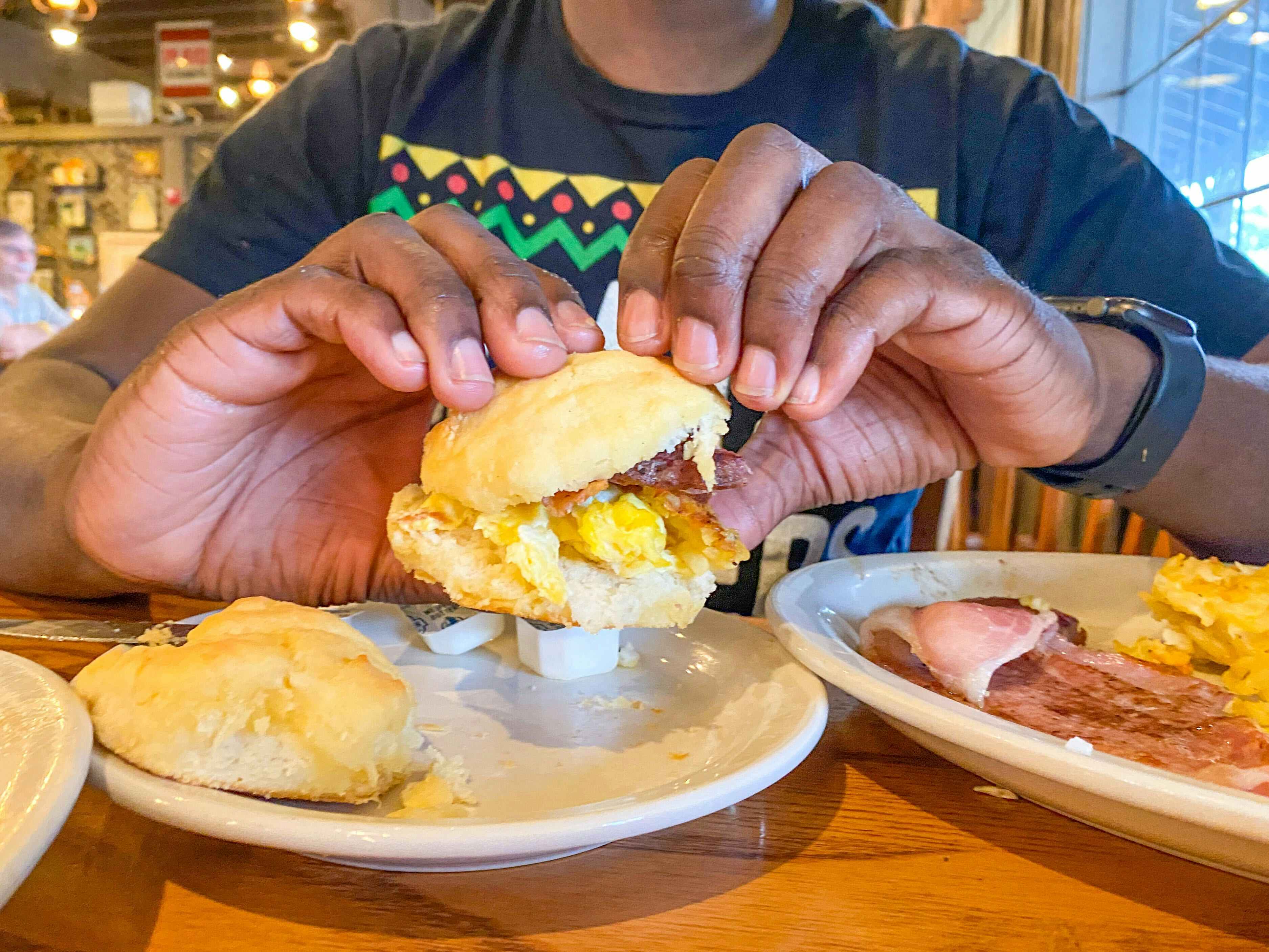 A person holding a breakfast sandwich above a plate on a table at Cracker Barrel.