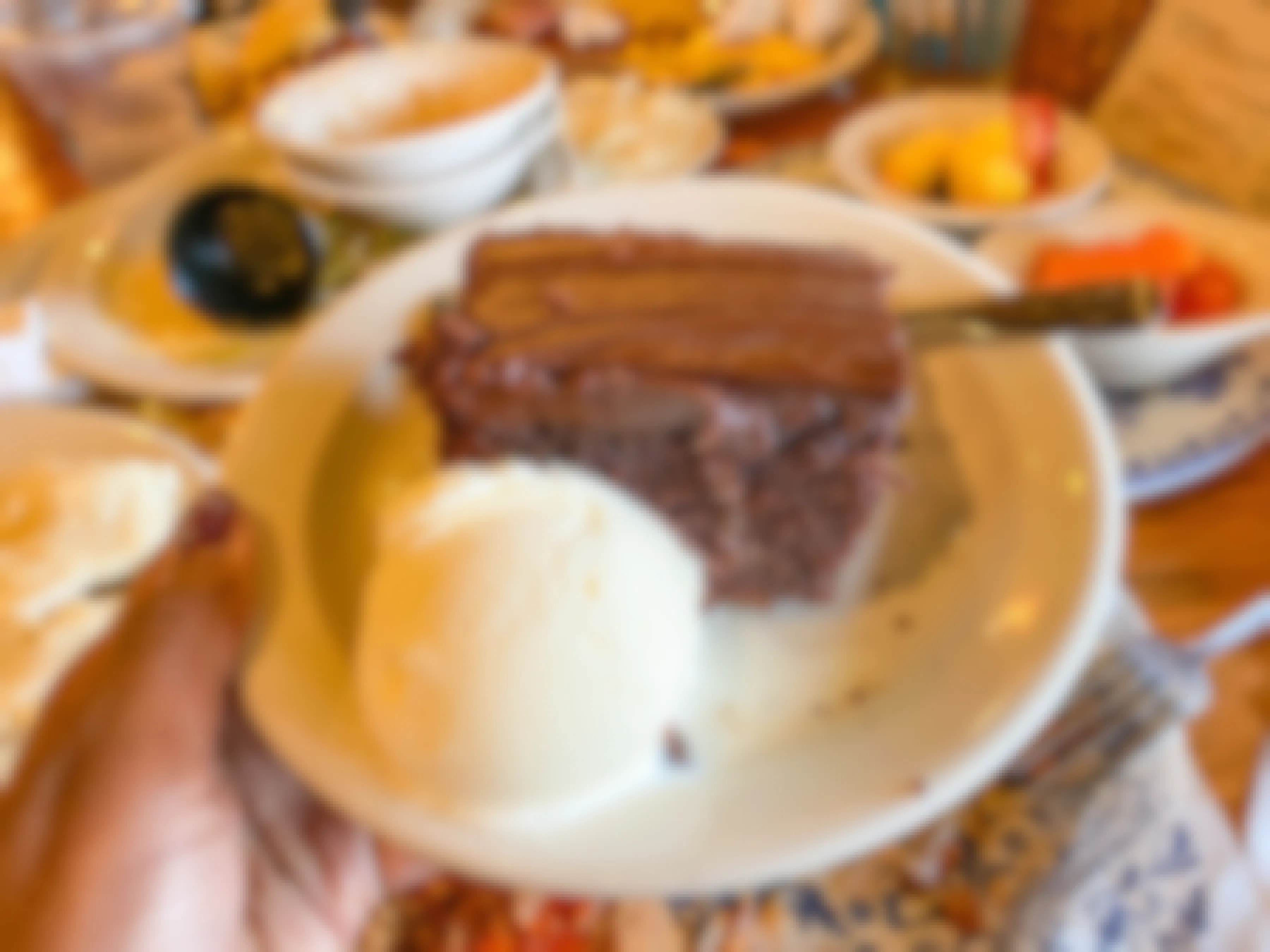 A person's hand holding up a plate with a Cracker Barrel brownie and ice cream dessert on it.