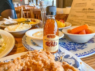 A small Cracker Barrel syrup bottle sitting on a table of food at Cracker Barrel.