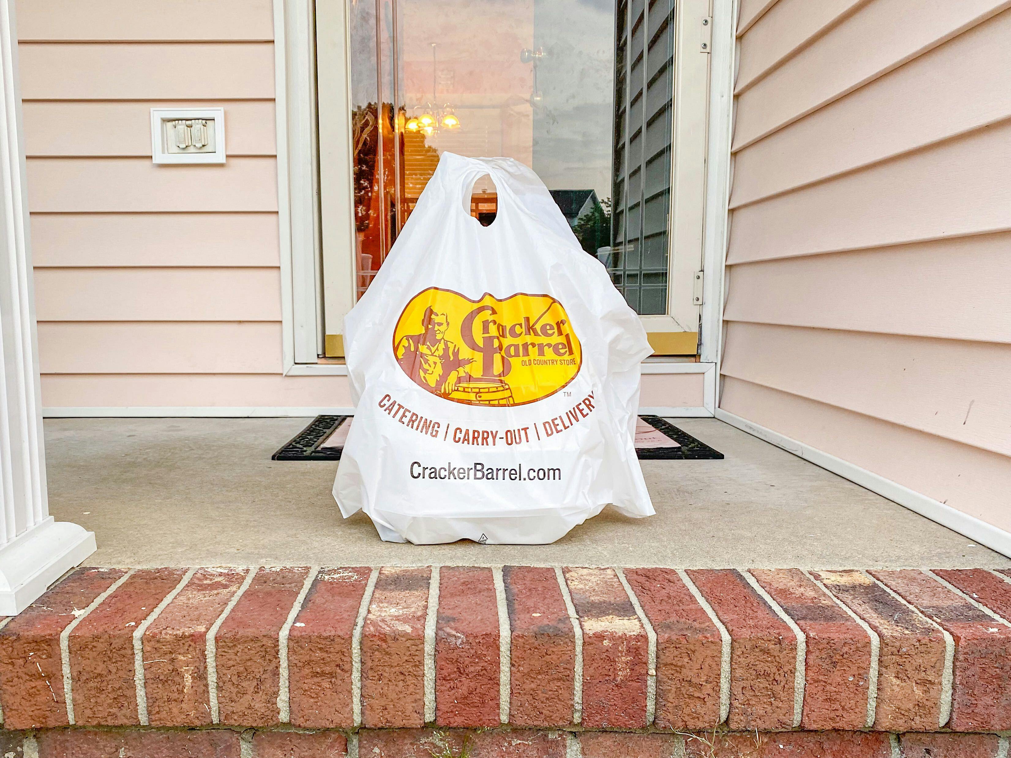 A Cracker Barrel takeout bag of food sitting on a front porch.