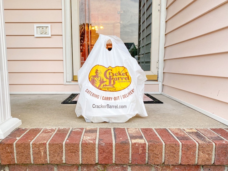 A Cracker Barrel takeout bag of food sitting on a front porch.