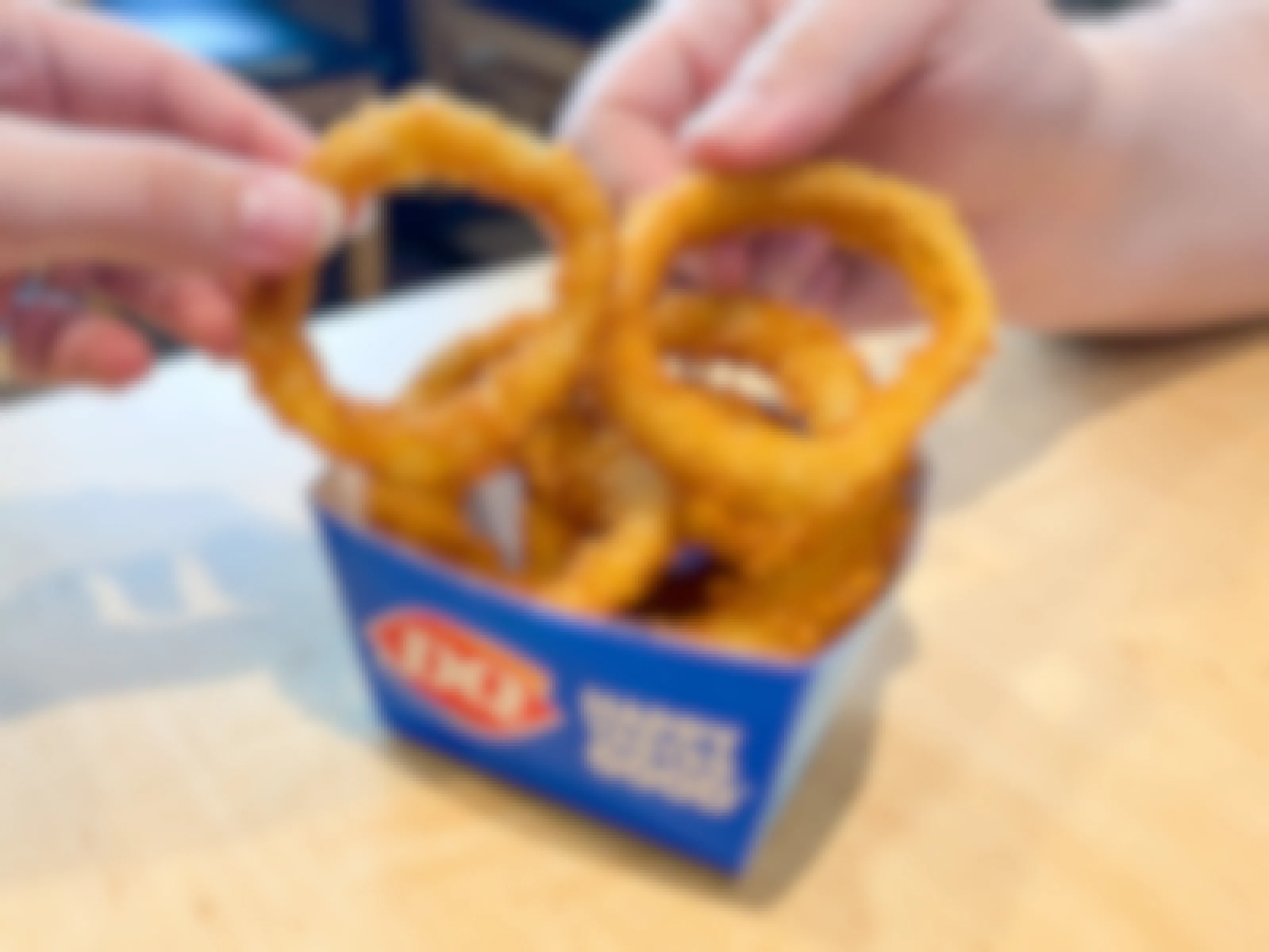 Two people's hands reaching in to each take an onion ring from a box of Dairy Queen onion rings sitting on a table inside Dairy Queen.