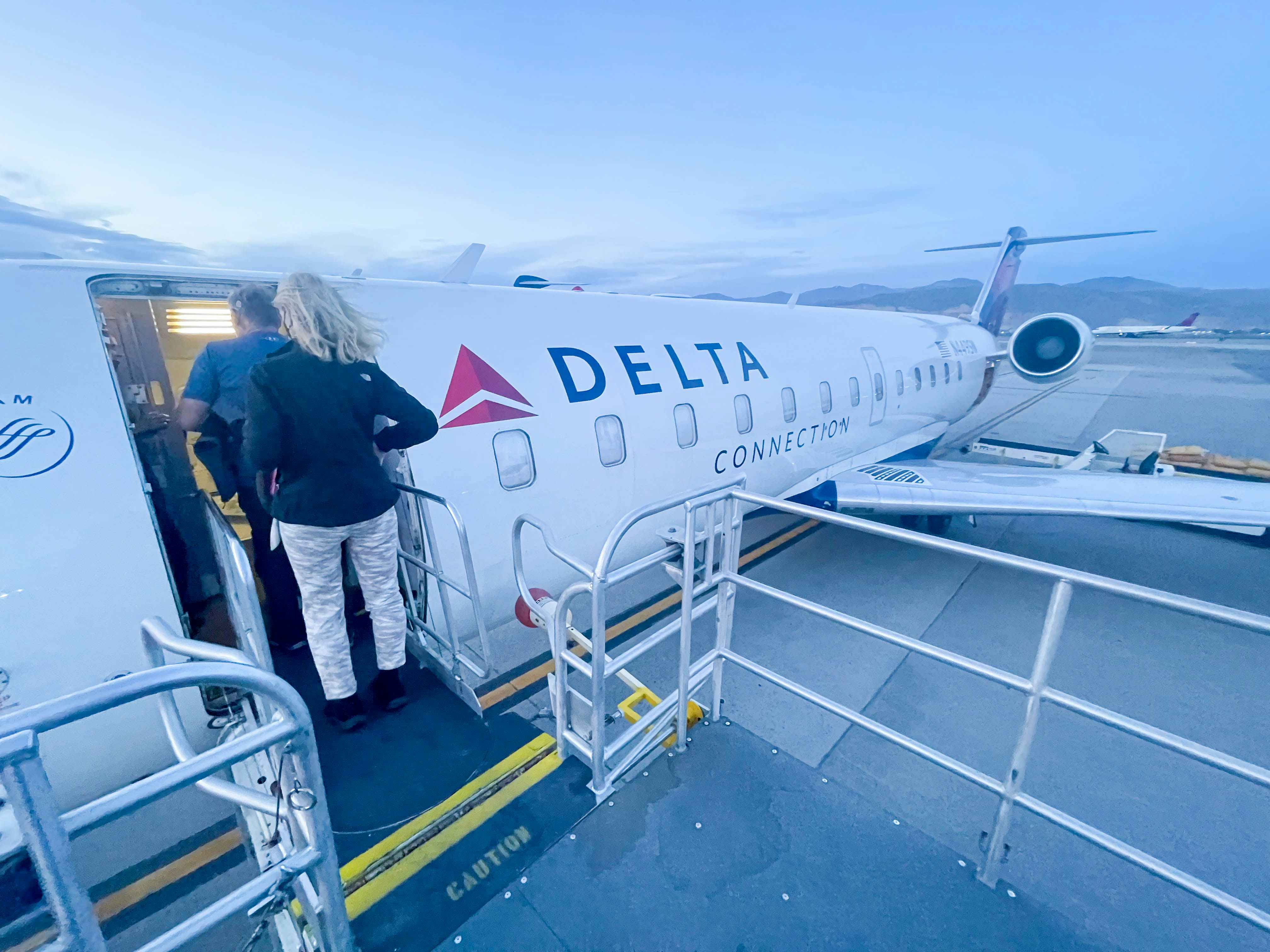 Two people walking onto a small Delta plane on a runway.