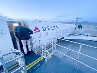 Two people walking onto a small Delta plane on a runway.