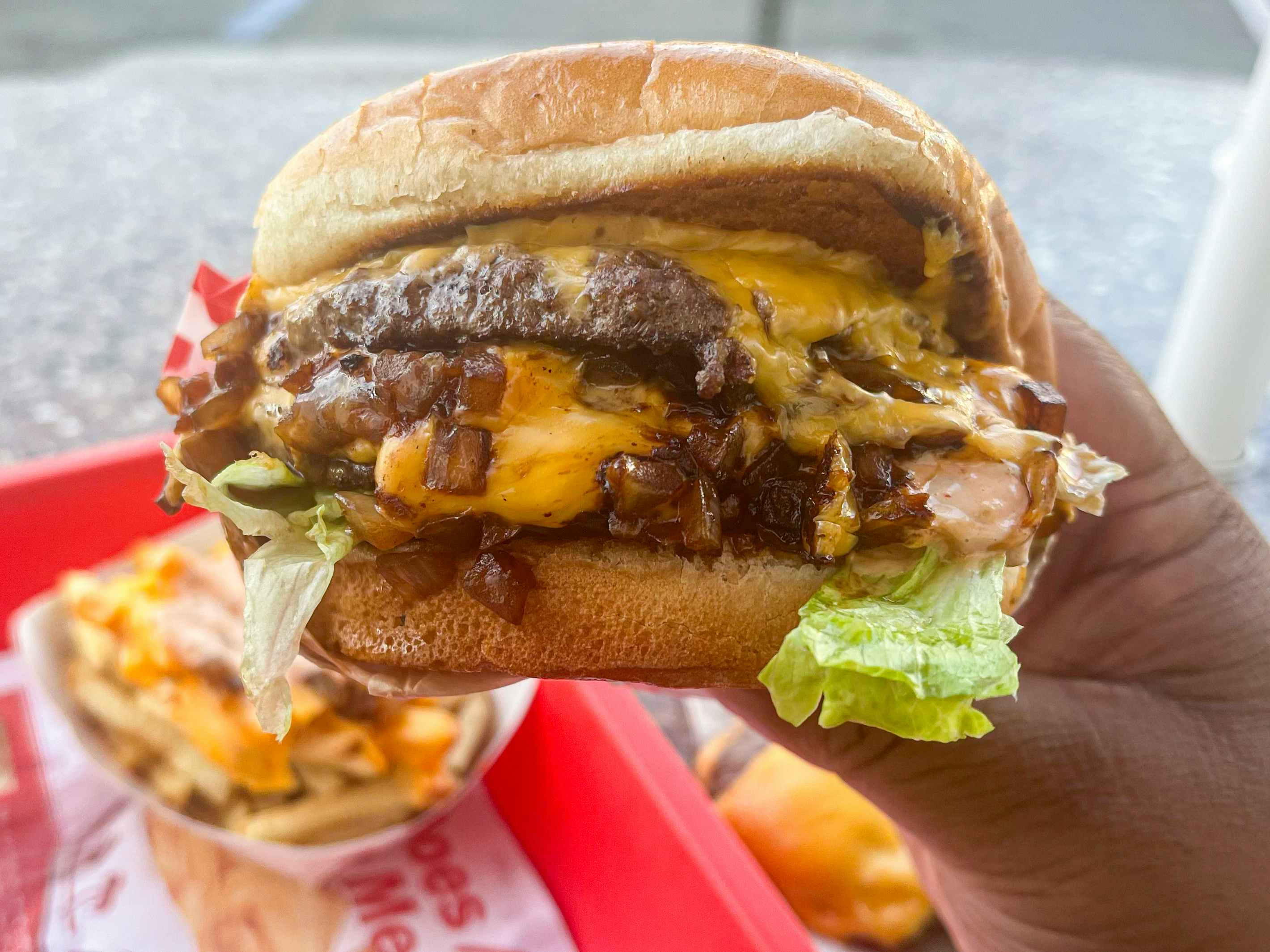 A person holding an in-n-out burger with cheese, onions, and multiple patties on it — "animal style" on the in n out secret menu