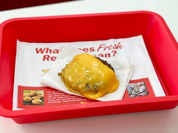 Two burger patties with melted cheese and no bun on a tray inside an In-N-Out restaurant, part of the in n out secret menu.