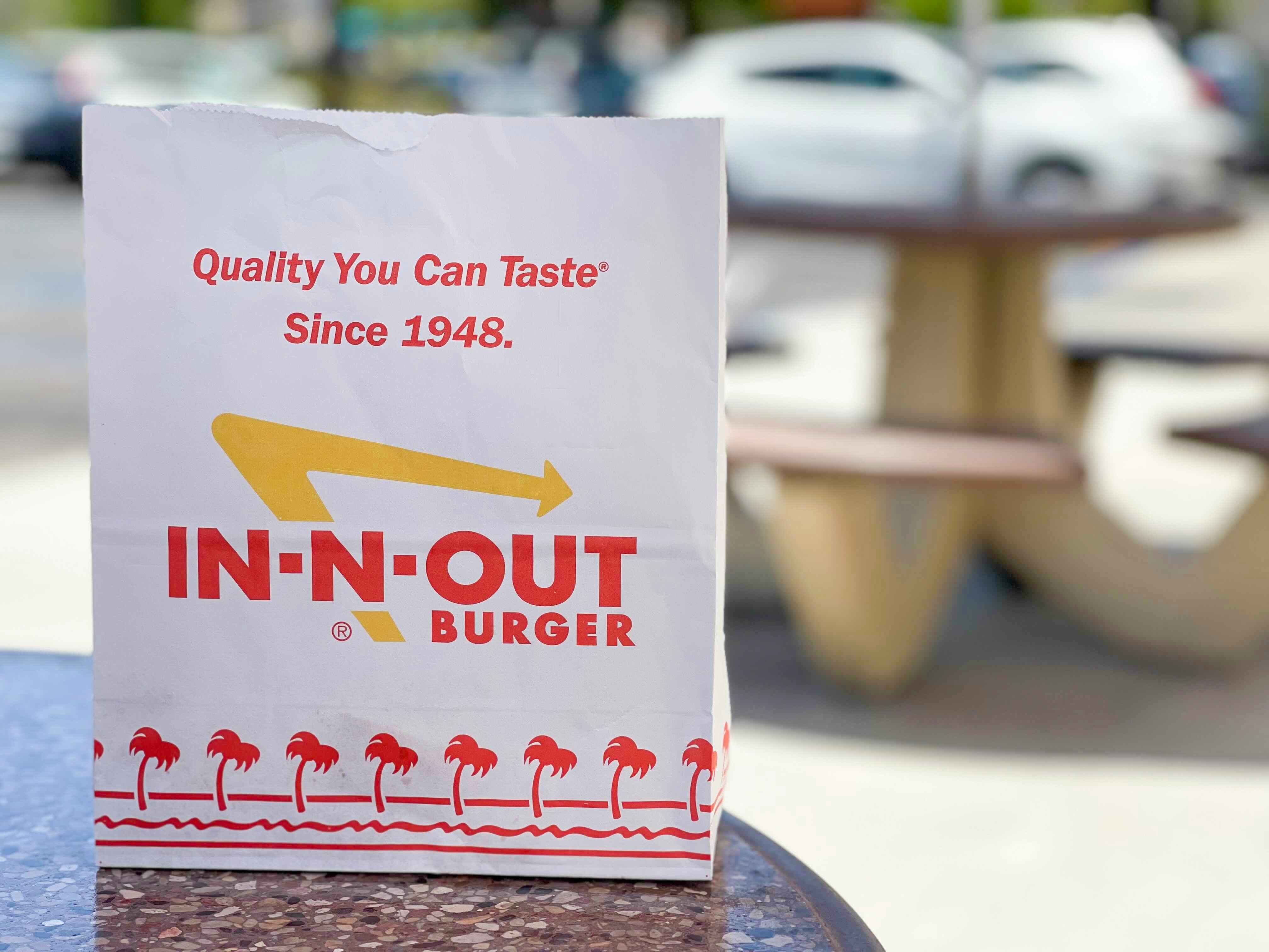 An In-N-Out to go bag sitting on a table outside of a restaurant.