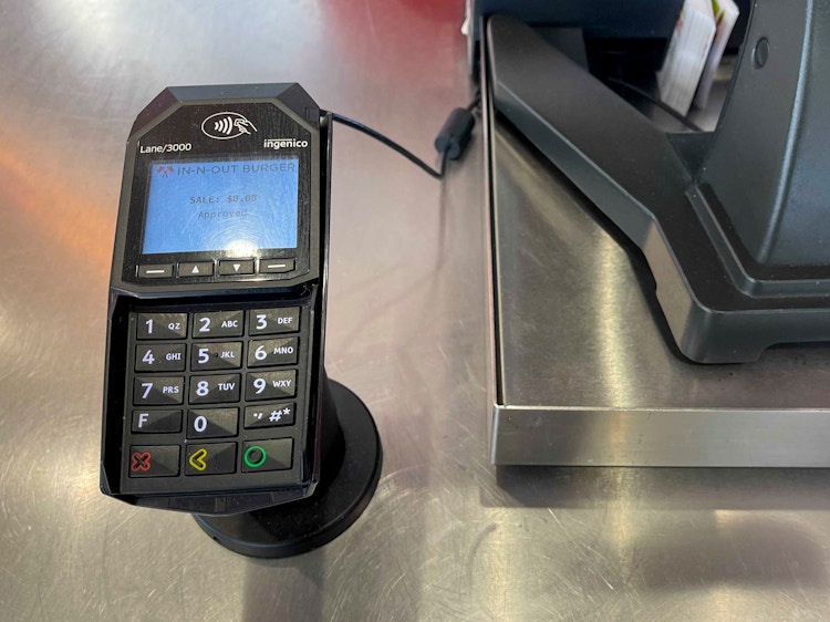 A credit card machine next to a cash register at the counter at In-N-Out.
