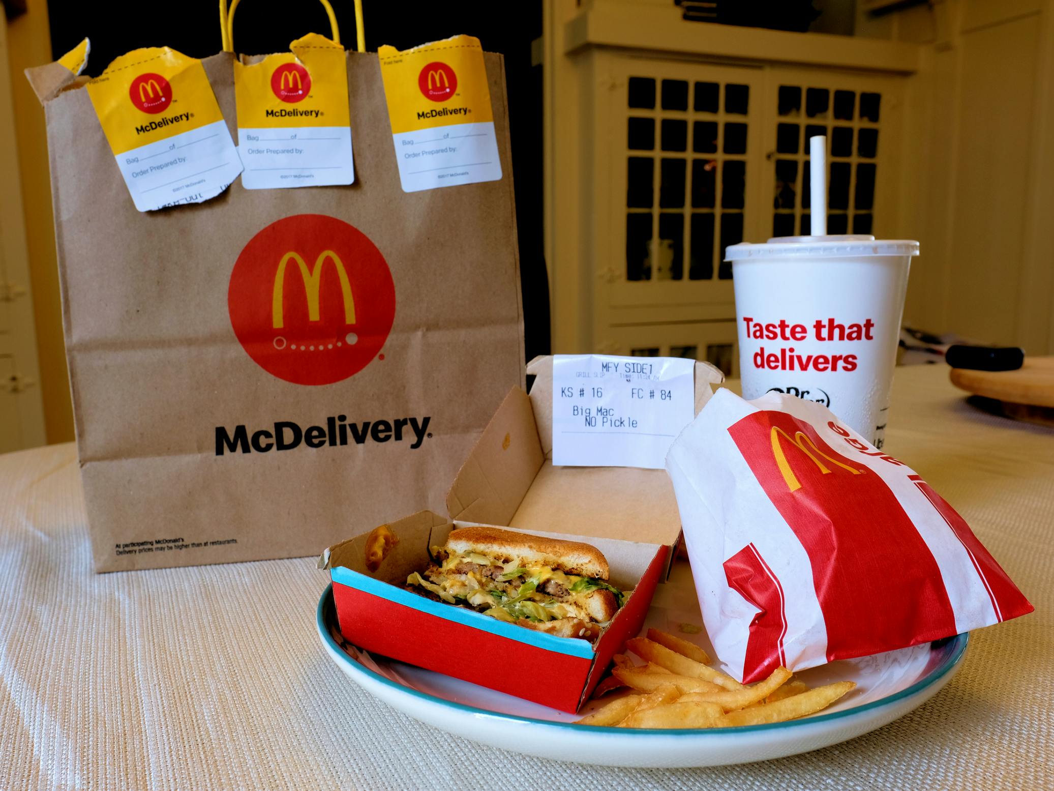 A Big Mac meal with fries and a drink sitting on a table next to a McDonald's McDelivery bag from Uber Eats.