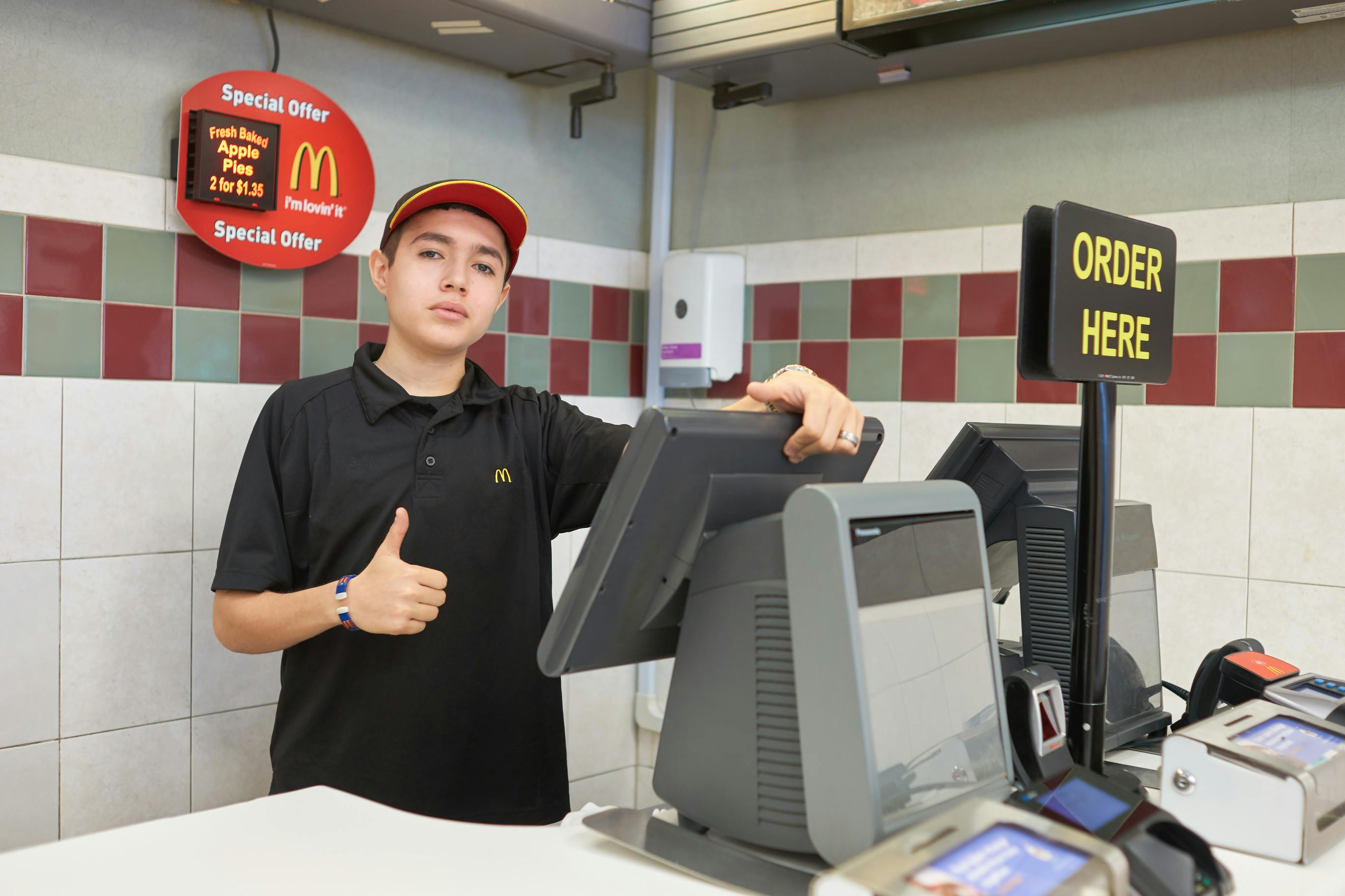 A McDonald's employee giving a thumbs up while standing behind the register at a McDonald's restaurant.