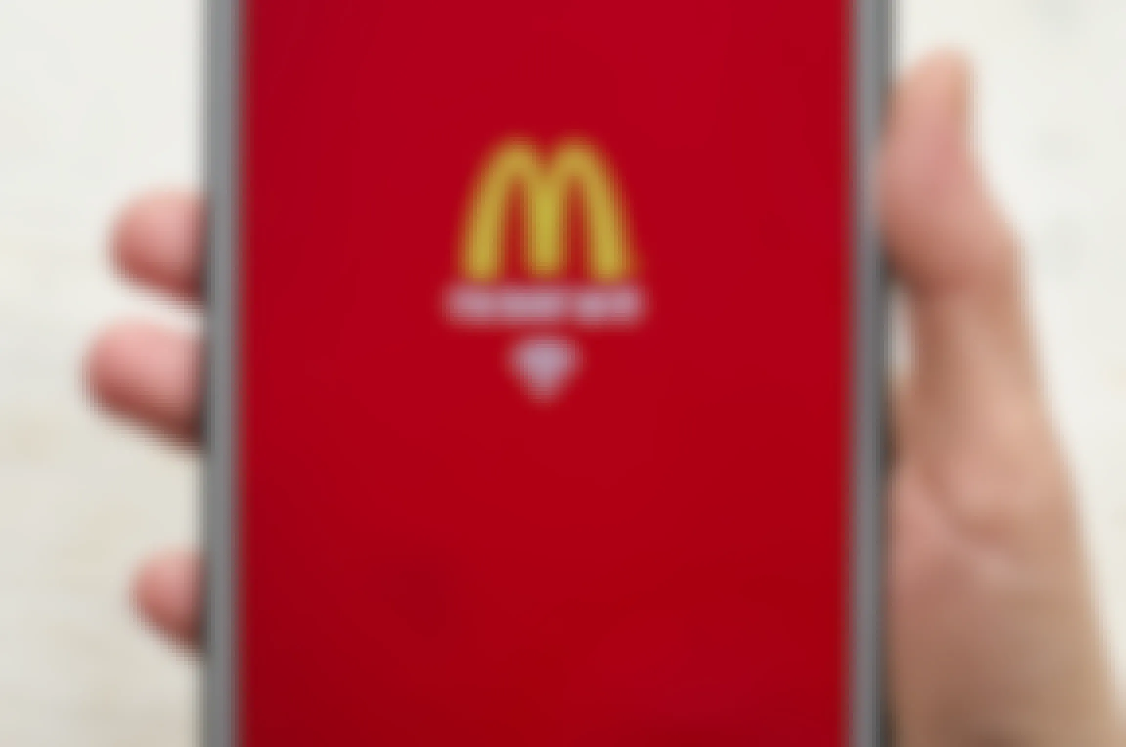 A person's hand holding a phone with the McDonald's app open showing the golden arches logo and reads "I'm lovin' wi-fi