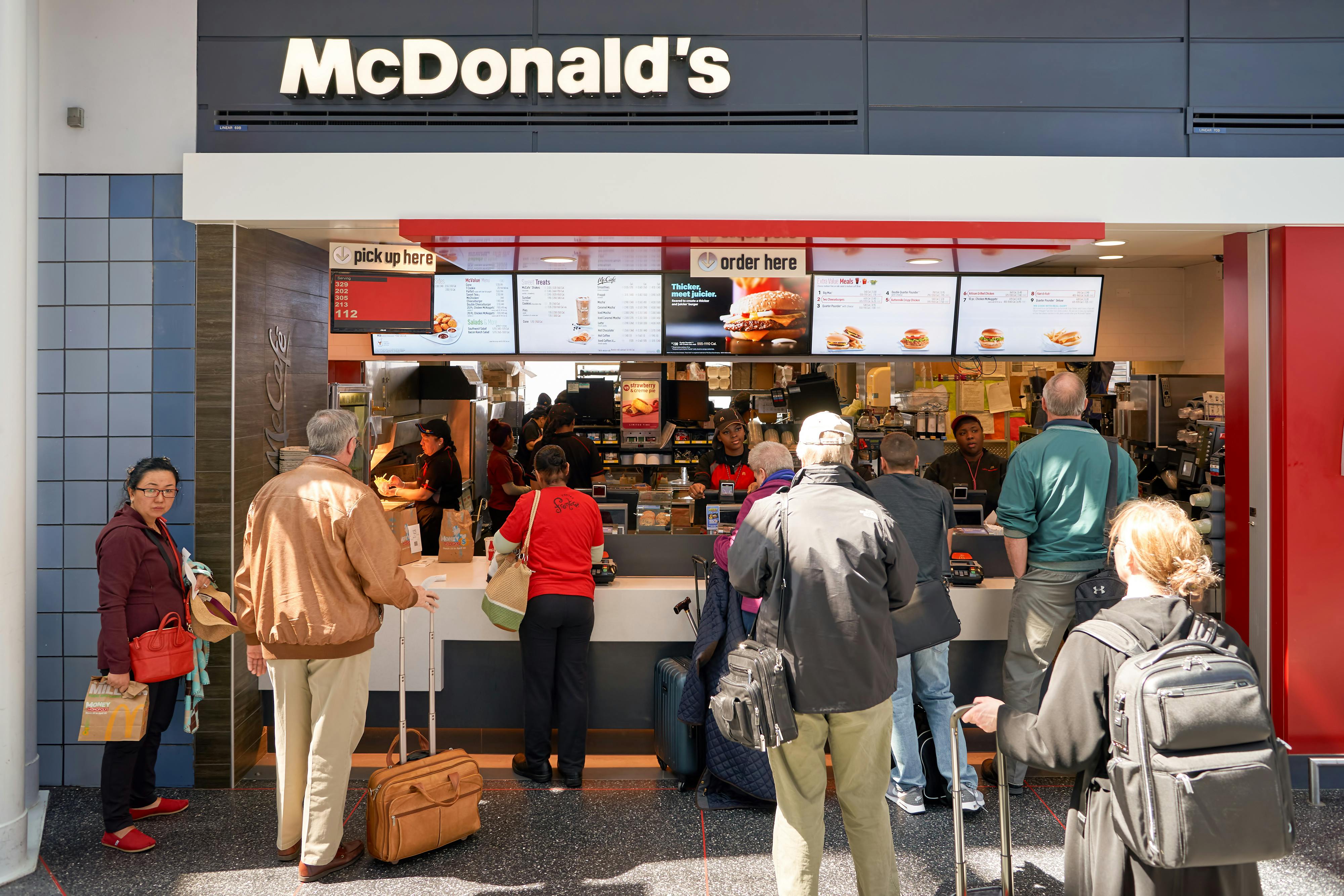 Senior-aged people waiting in line at the McDonald's restaurant counter inside an airport.