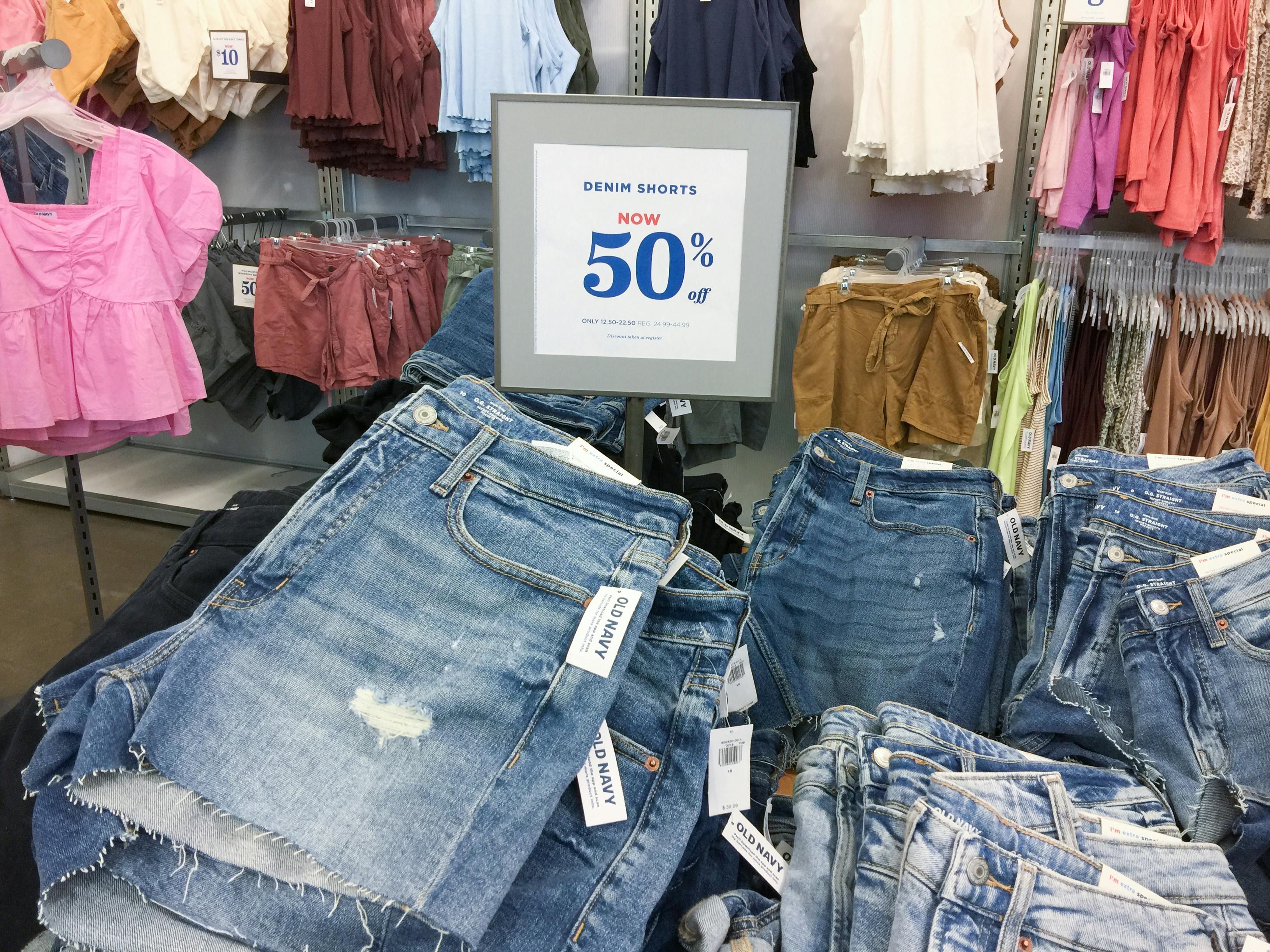A table of denim shorts inside Old Navy, with a sign that reads, "Denim shorts, now 50% off