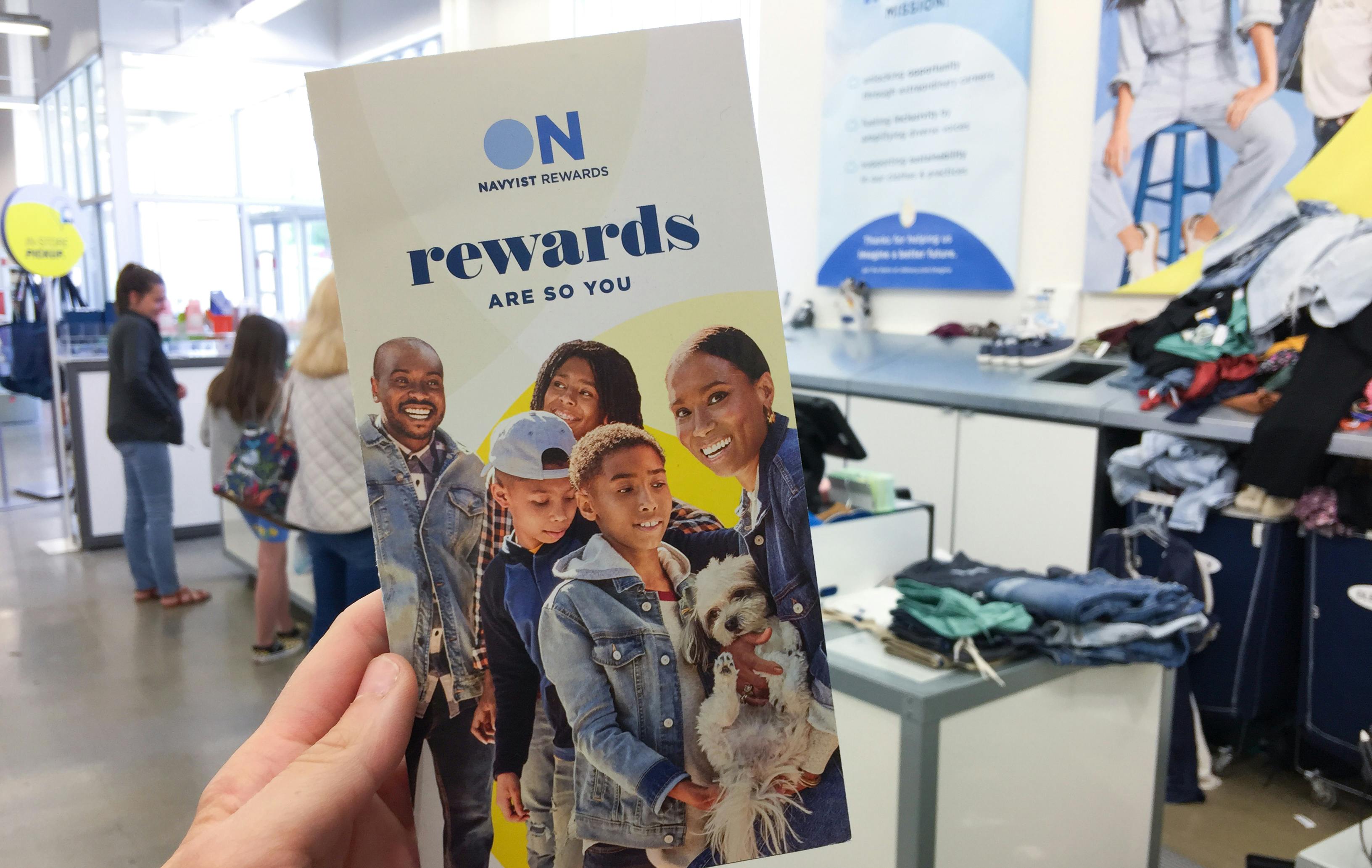 A person's hand holding up a brochure for Old Navy's reward program while standing in line for checkout at Old Navy.