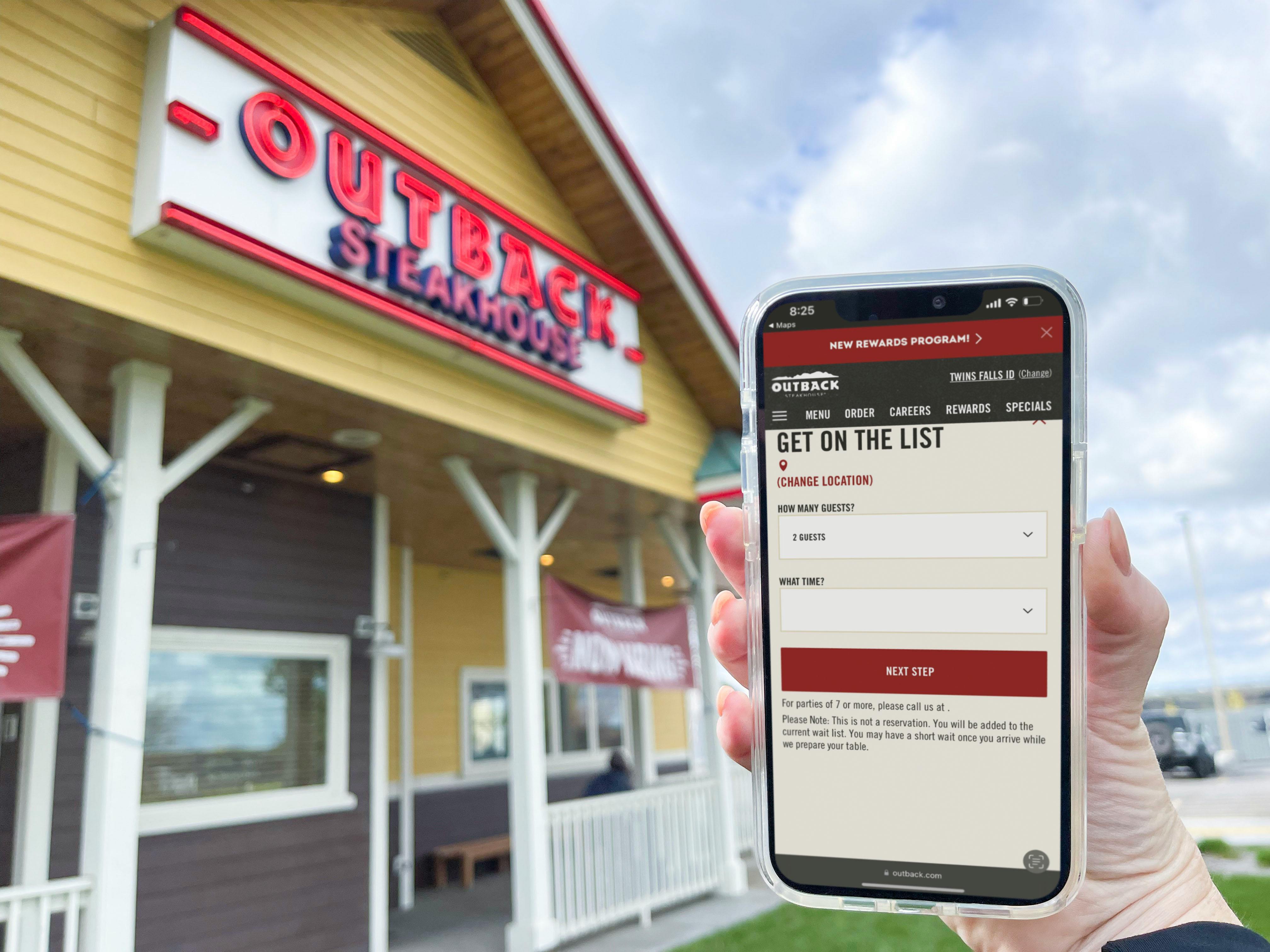 A person's hand holding up a cell phone displaying the Outback Steakhouse online waitlist form in front of an Outback Steakhouse restaurant.