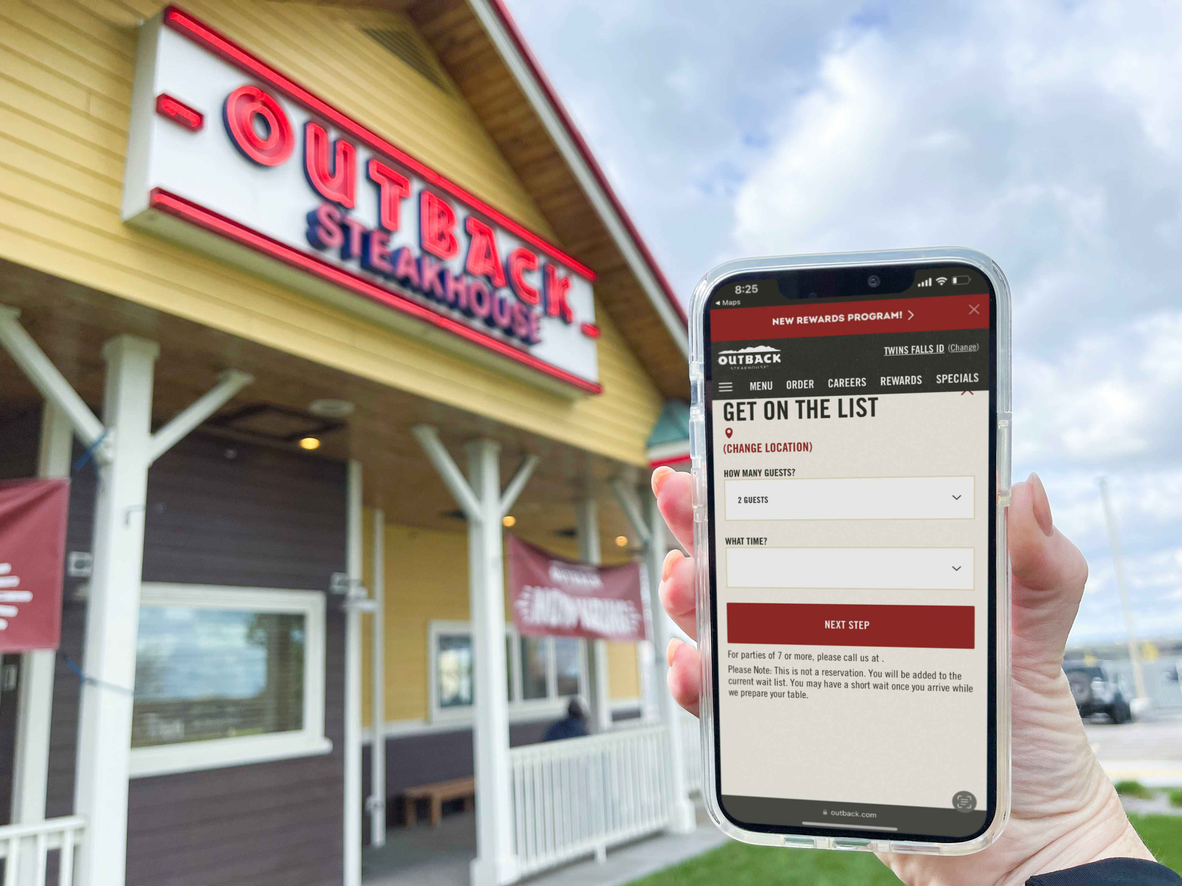 A person's hand holding up a cell phone displaying the Outback Steakhouse online waitlist form in front of an Outback Steakhouse restaurant.