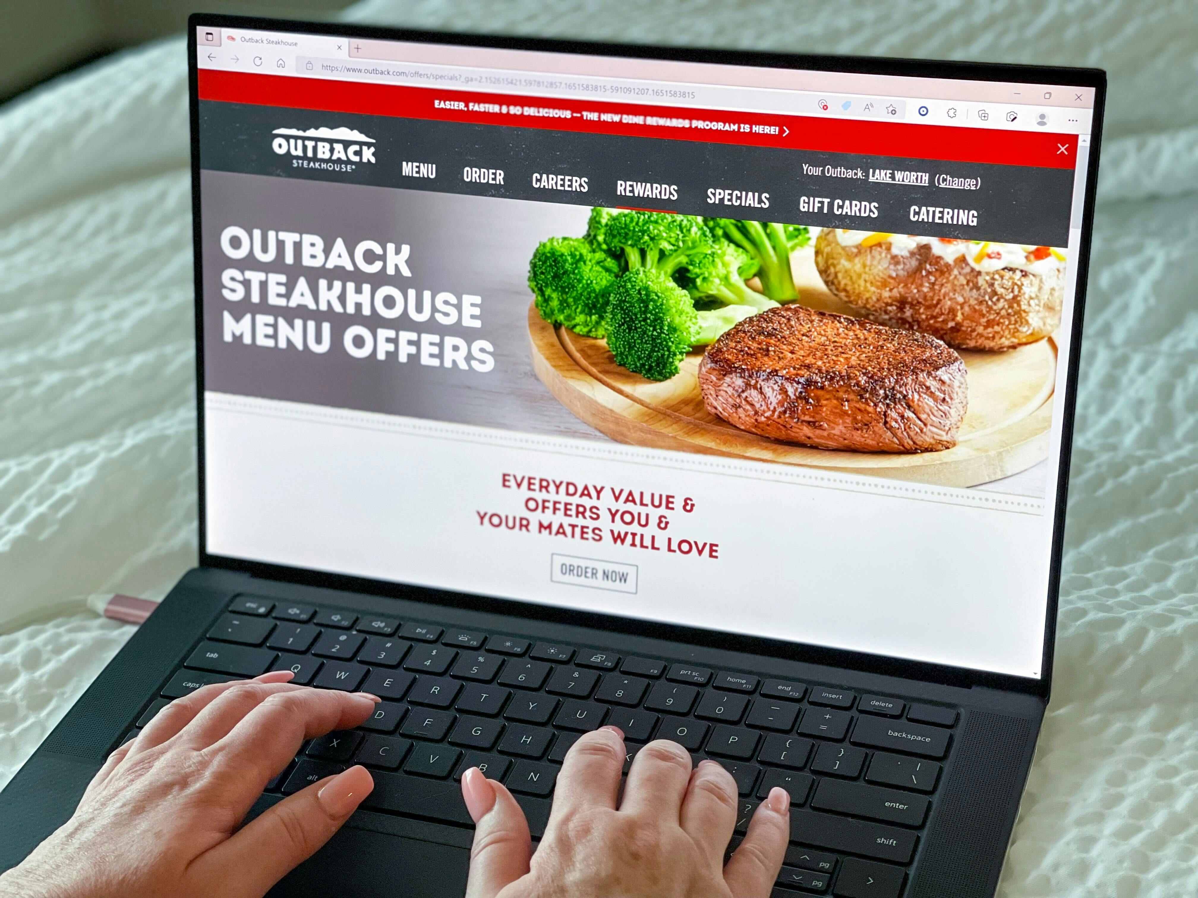 A person's hands using a laptop that is displaying the Outback Steakhouse specials webpage.