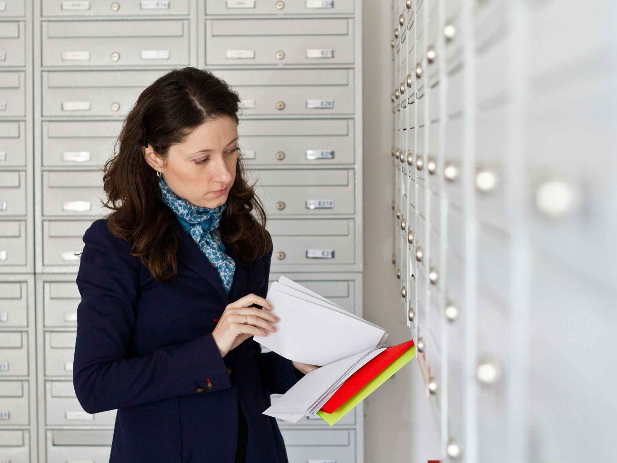 a person standing at a wall of mail boxes, looking through a handful of envelopes.