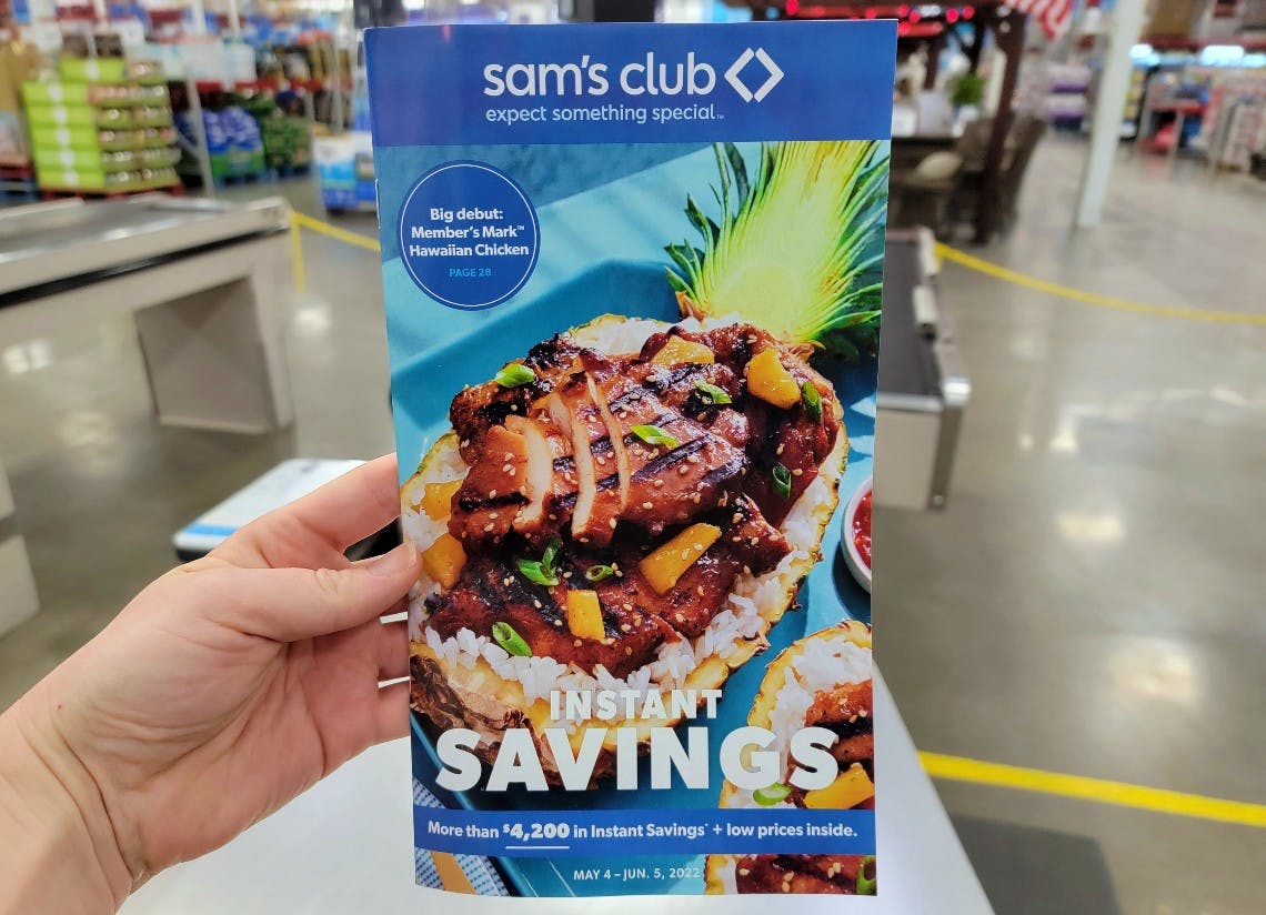 a person's hand holding the Sam's Club Instant Savings book from May 2022