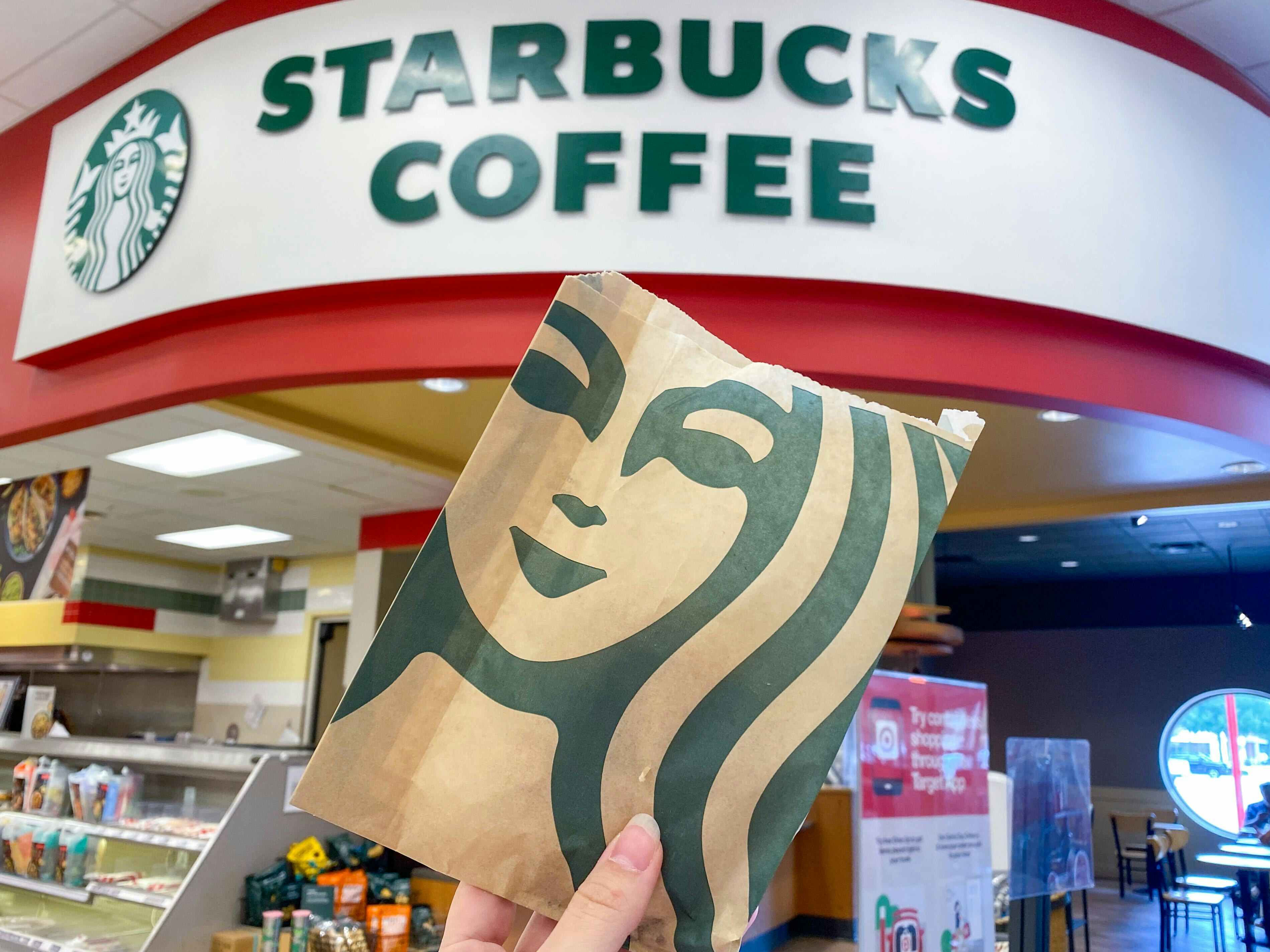 A person's hand holding up a Starbucks bag in front of the Starbucks Coffee sign inside Target.