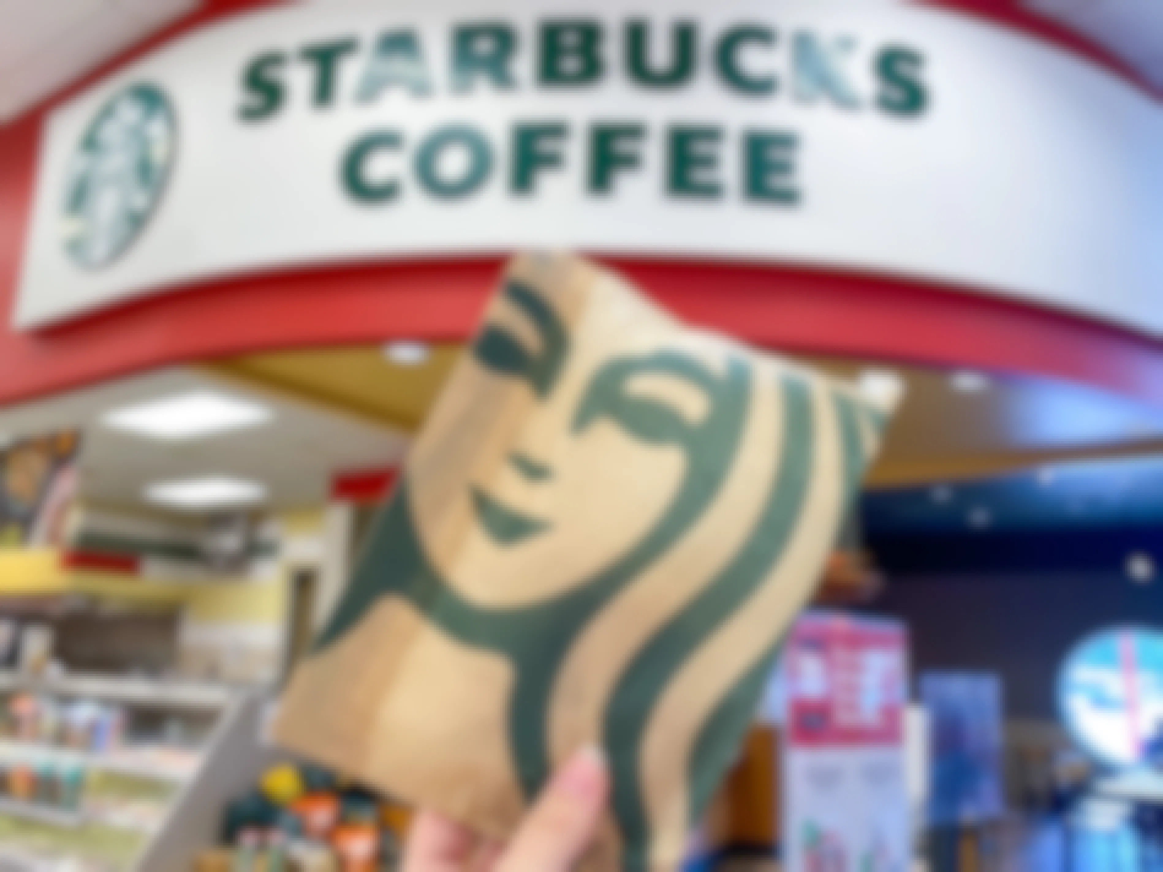 A person's hand holding up a Starbucks bag in front of the Starbucks Coffee sign inside Target.