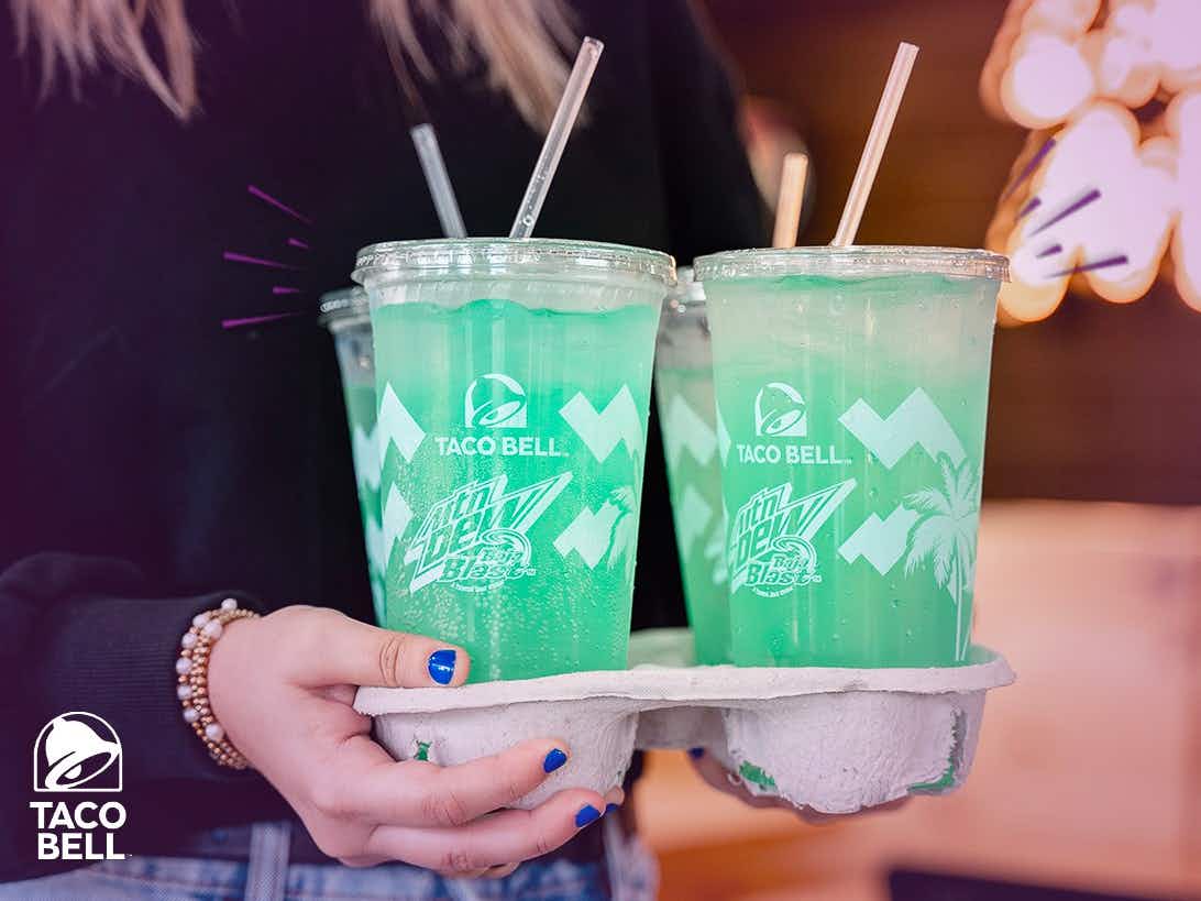 A person holding a cardboard drink holder with four Baja Blasts from Taco Bell.