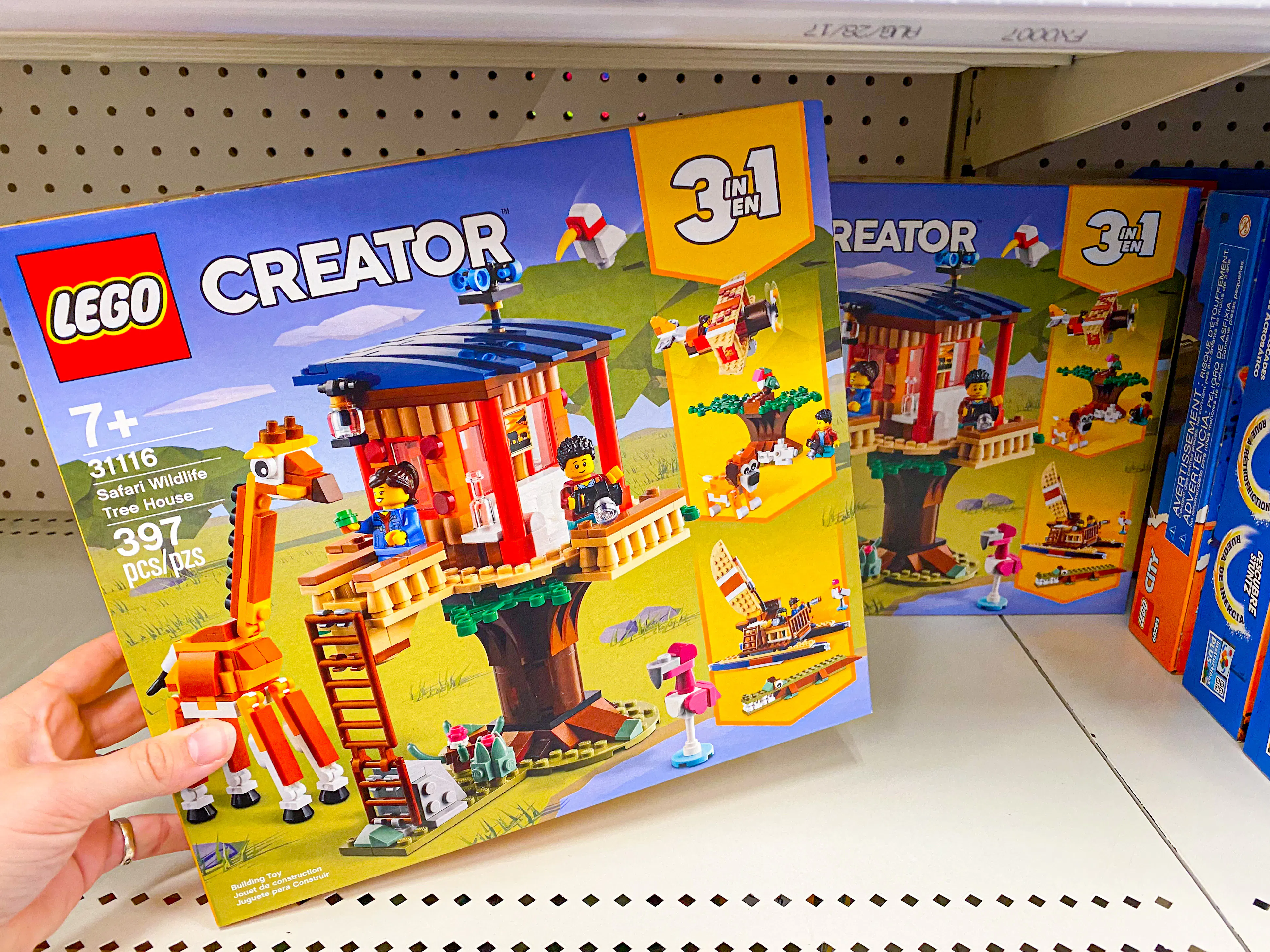 A person's hand taking a LEGO Creator 3-in-1 Safari Wildlife Tree House box set from a shelf in the LEGO toy aisle at Target.