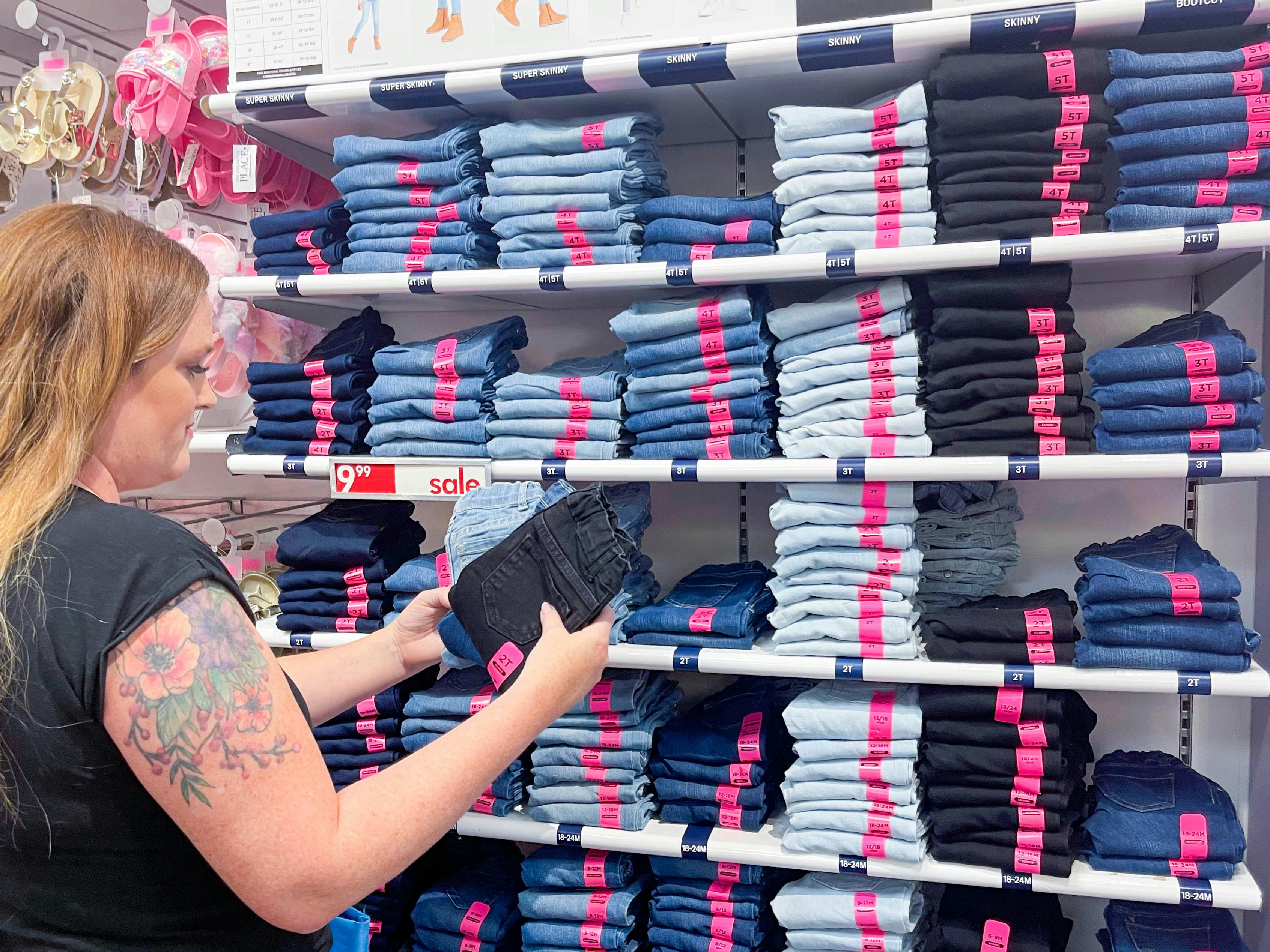 A woman looking at kids jeans in front of a Wall of different jeans at A Children's Place. 