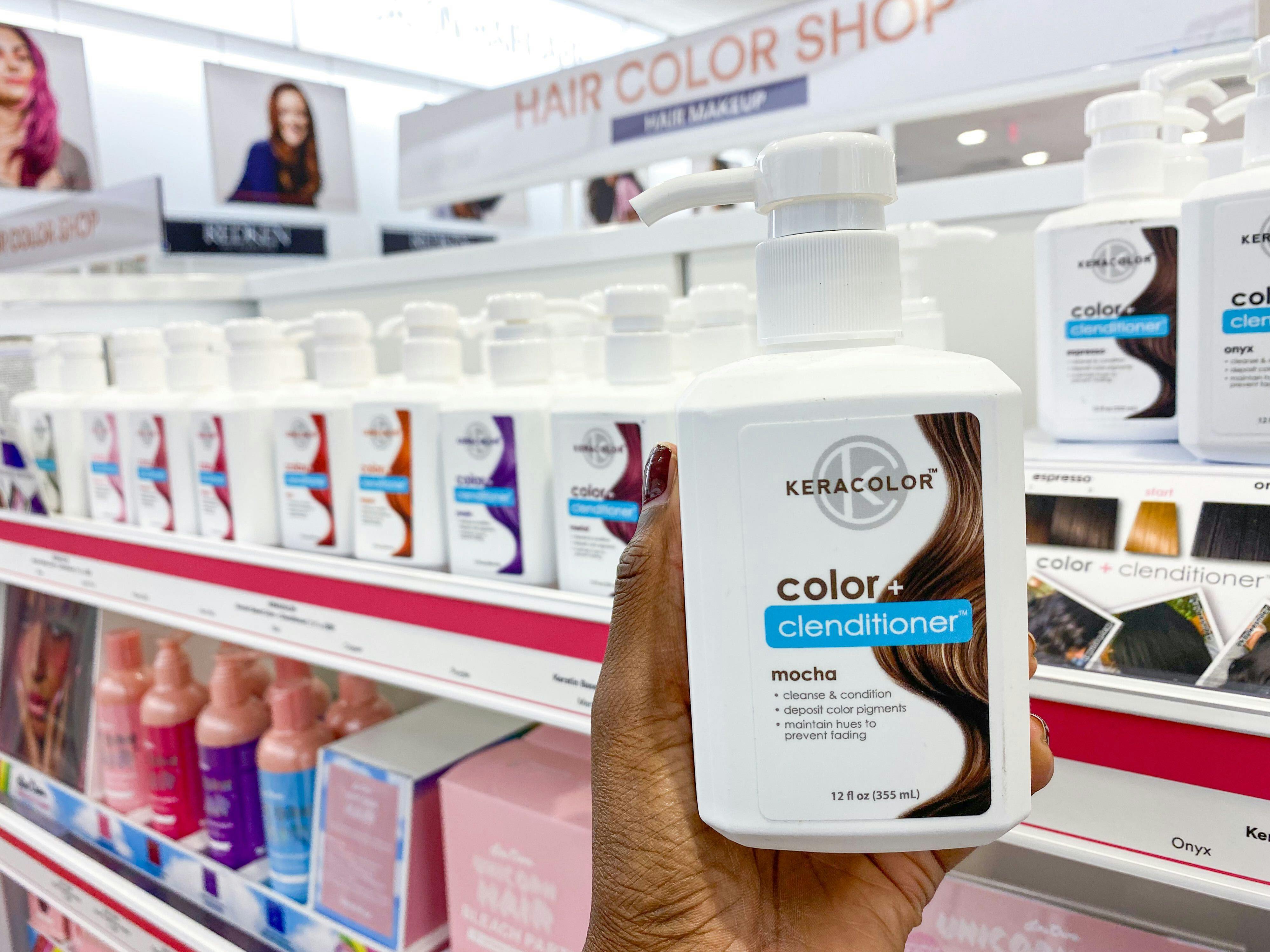 A person holding up a bottle of Keracolor + clenditioner in front of a shelf of different shades of the same product in Ulta.