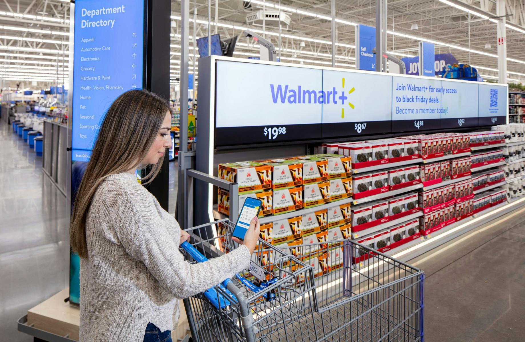 A woman on the Walmart app, pushing a cart, at the front of a Walmart store.