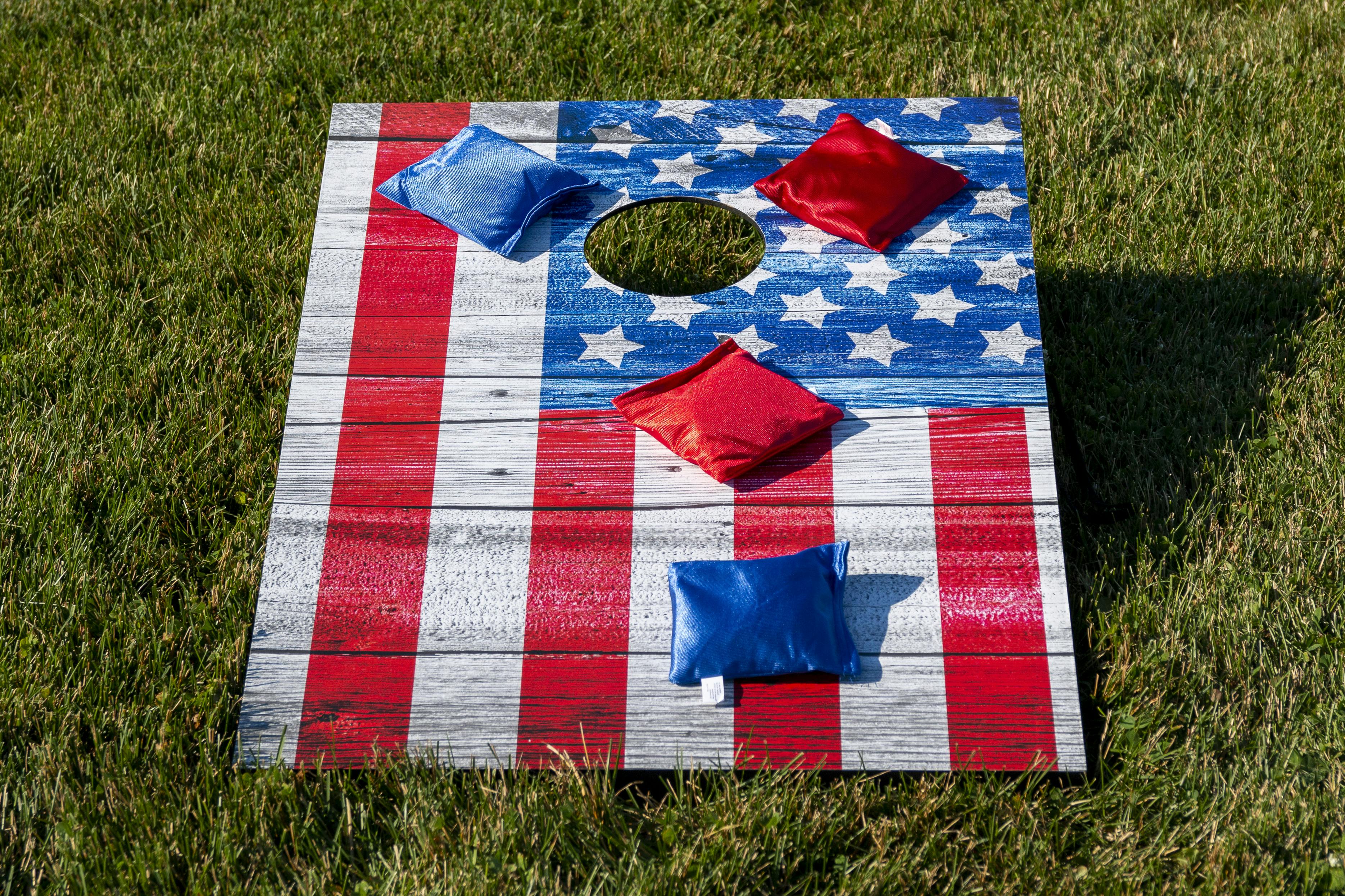 A cornhole goal painted to look like an American flag sitting on a lawn with red and blue bean bags on top of it.