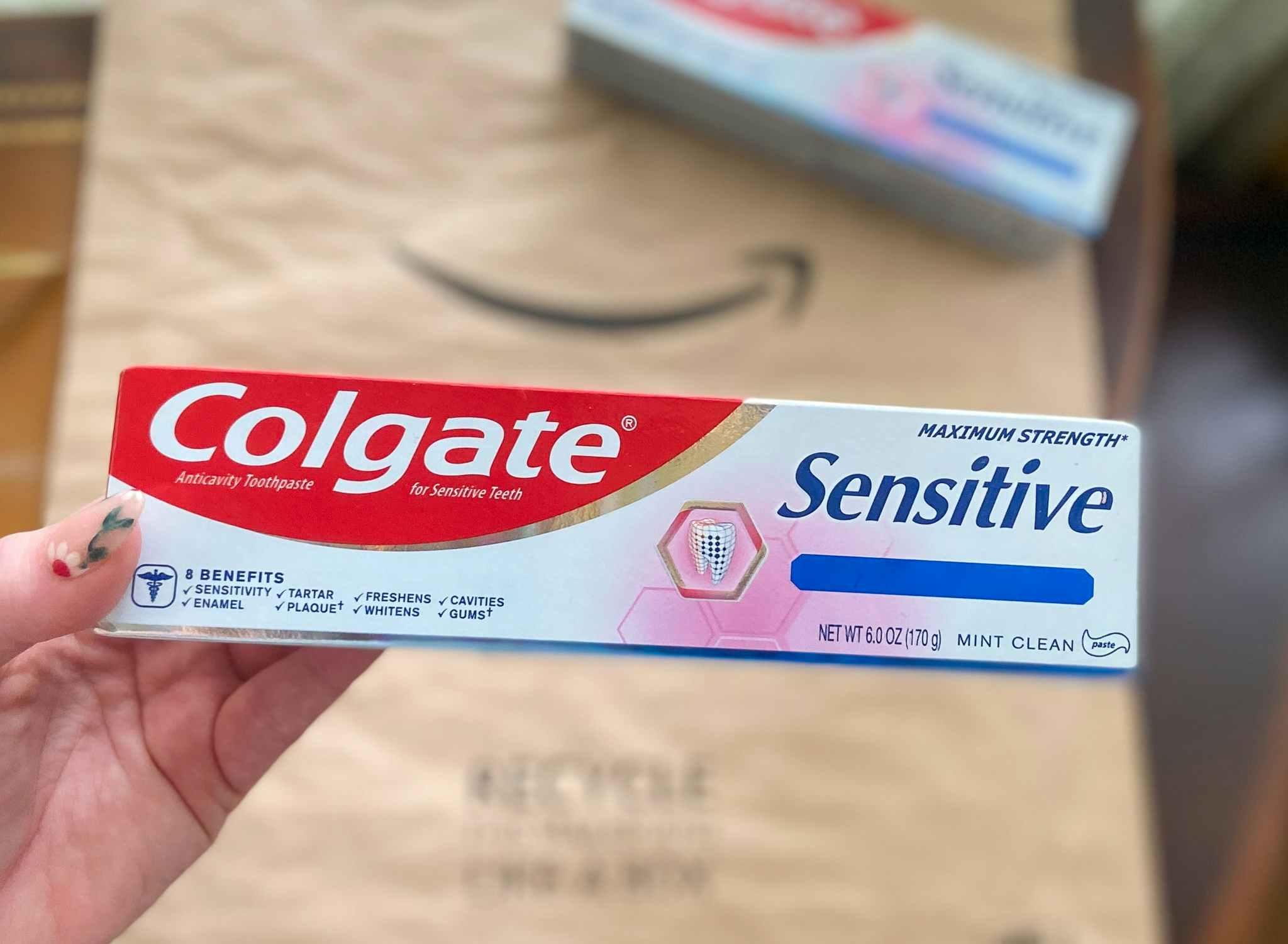 hand holding a tube of colgate sensitive toothpaste over an amazon logo package