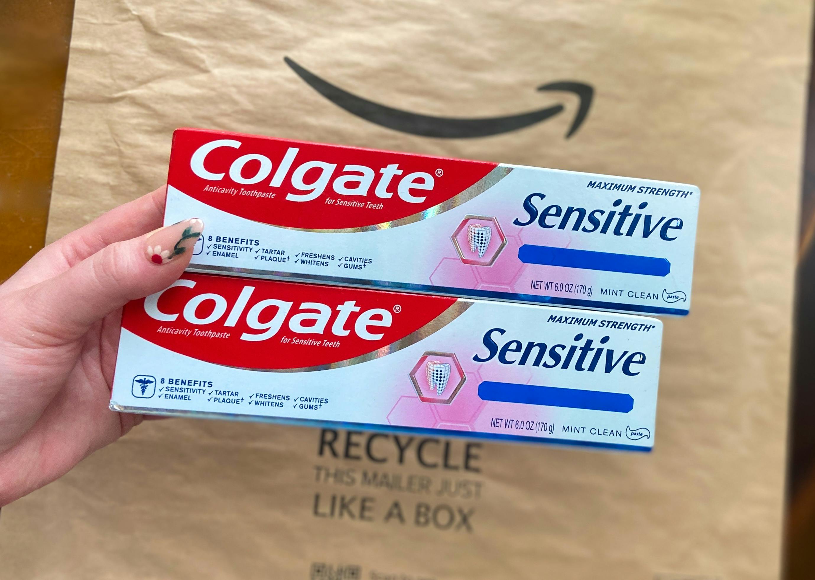 hand holding two tubes of colgate sensitive toothpaste over an amazon logo package