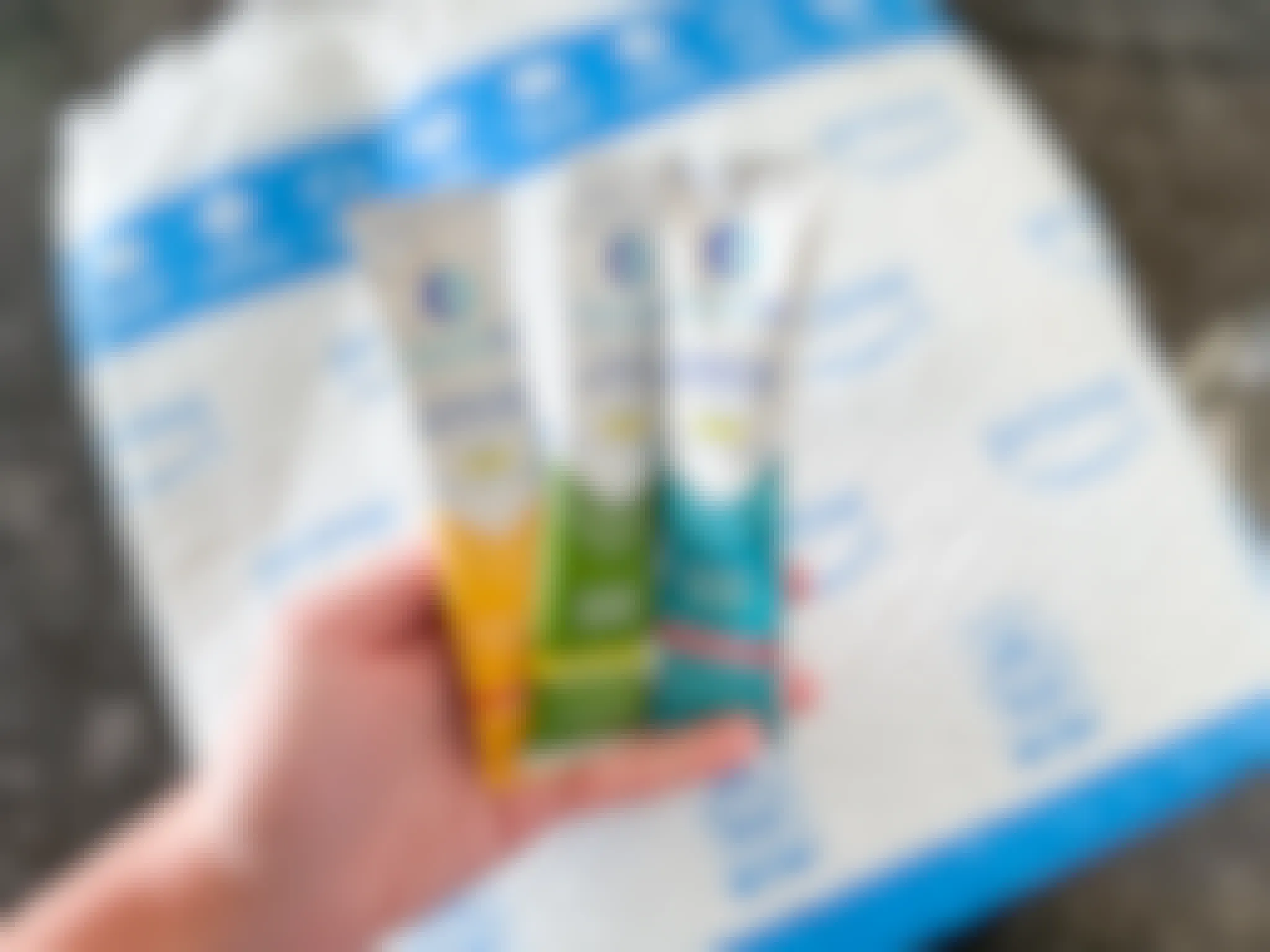 A hand holding three Liquid IV packets with an Amazon package in the background