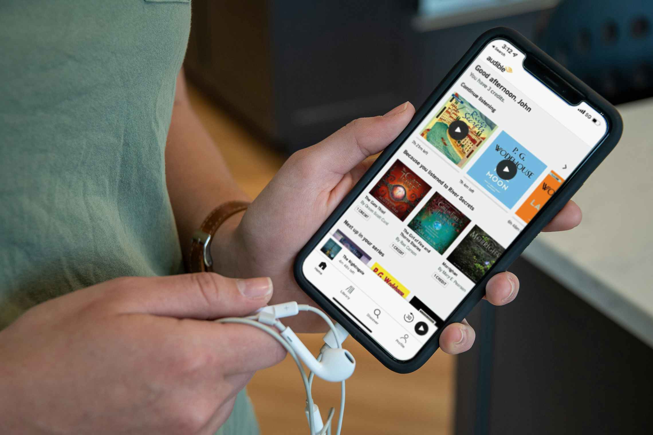 person with headphones and phone showing amazon audible audiobook marketplace