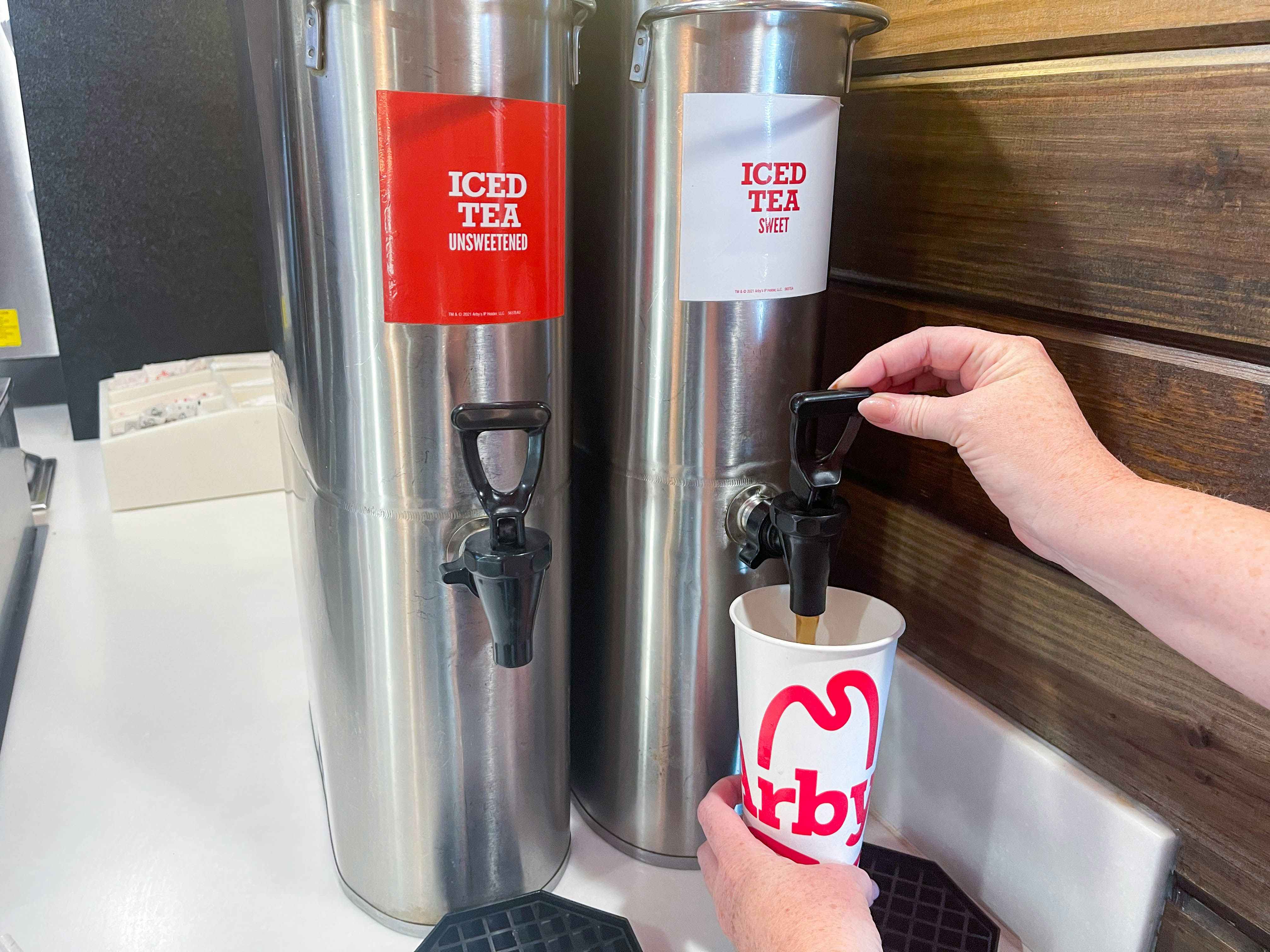 a person filling an arbys drink cup with iced tea 