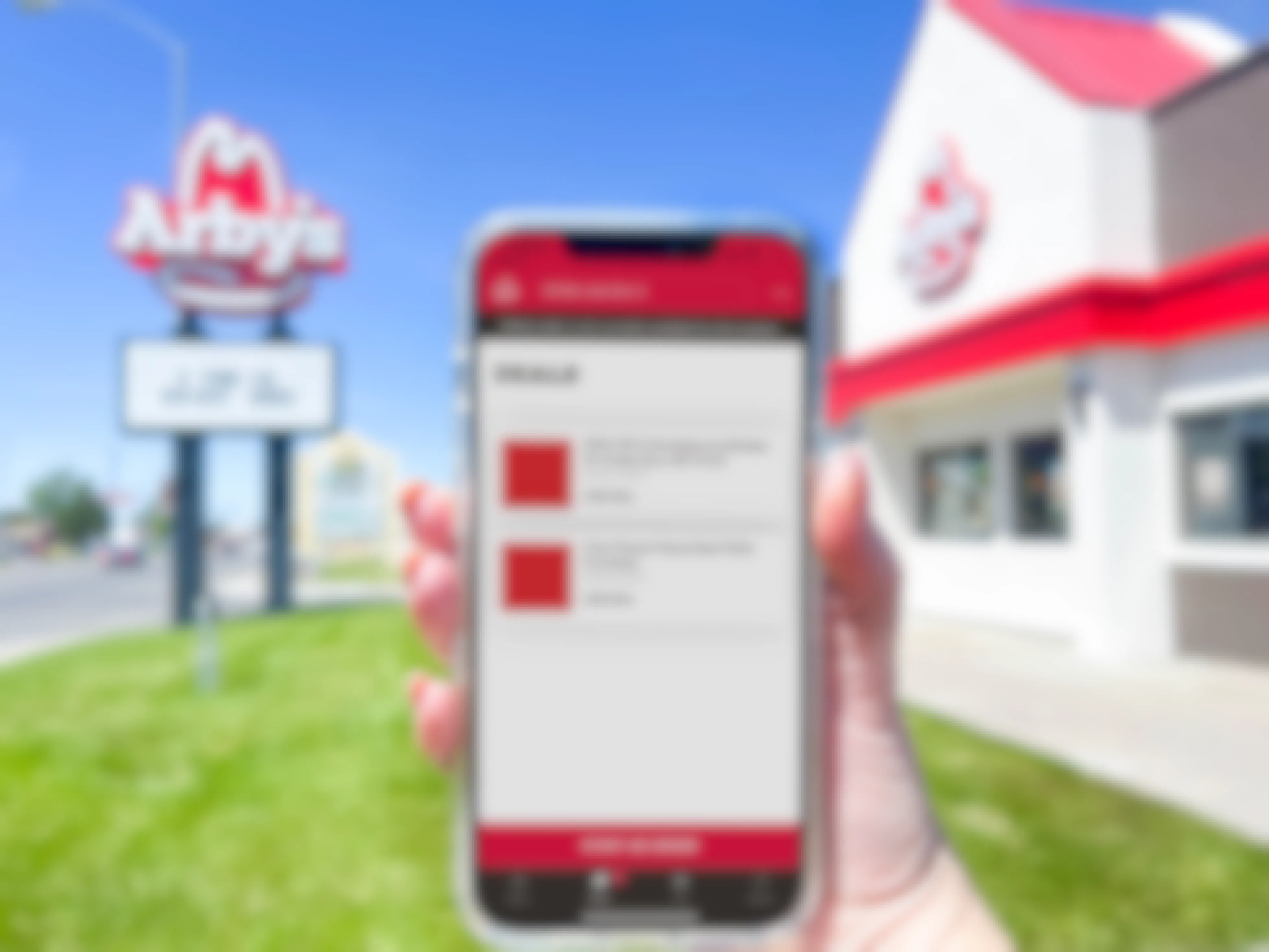 a cellphone being held in front of arbys in front with the arbys app deal page 