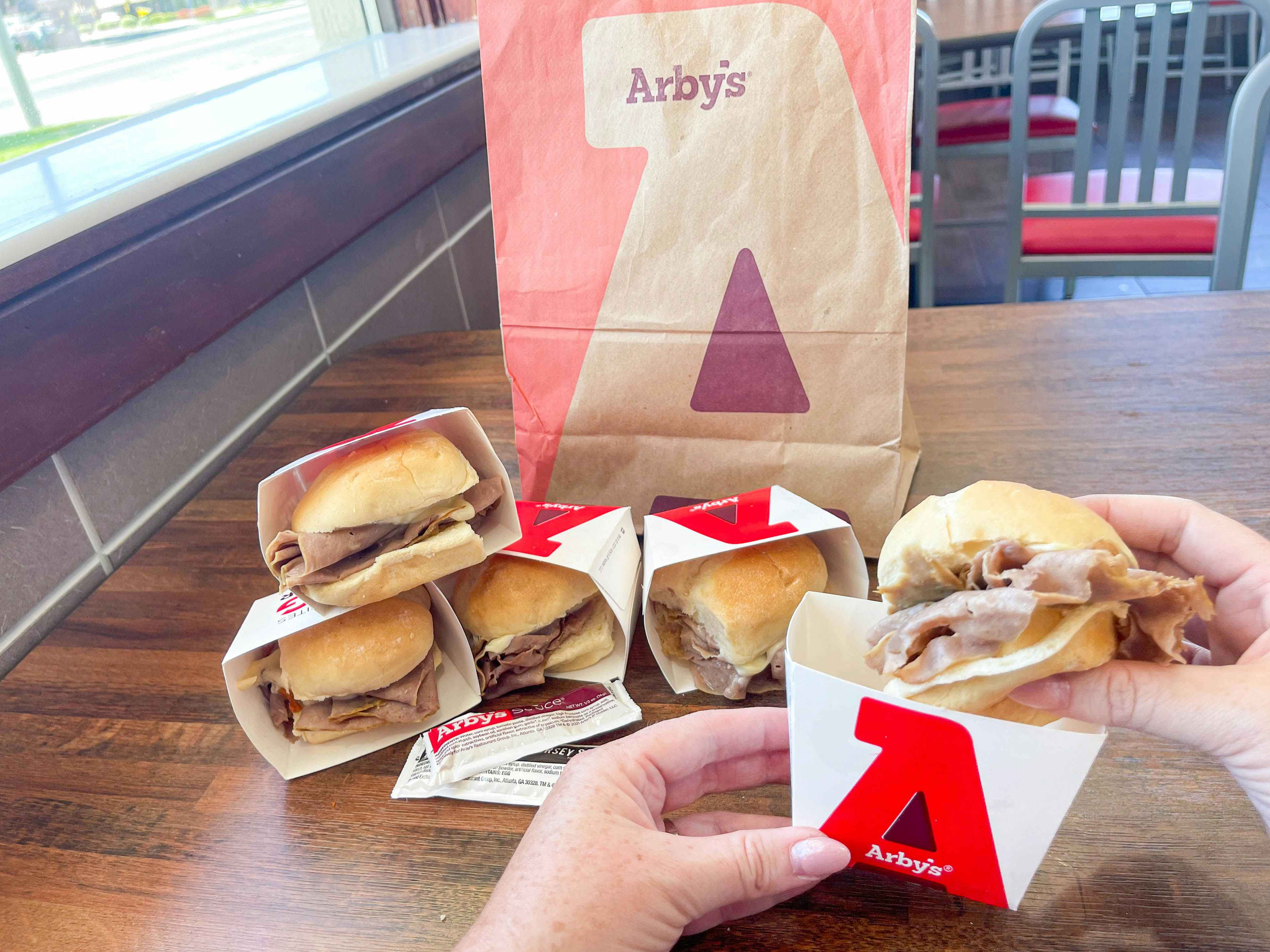 five roast beef slider on a table in front of a to go bag 