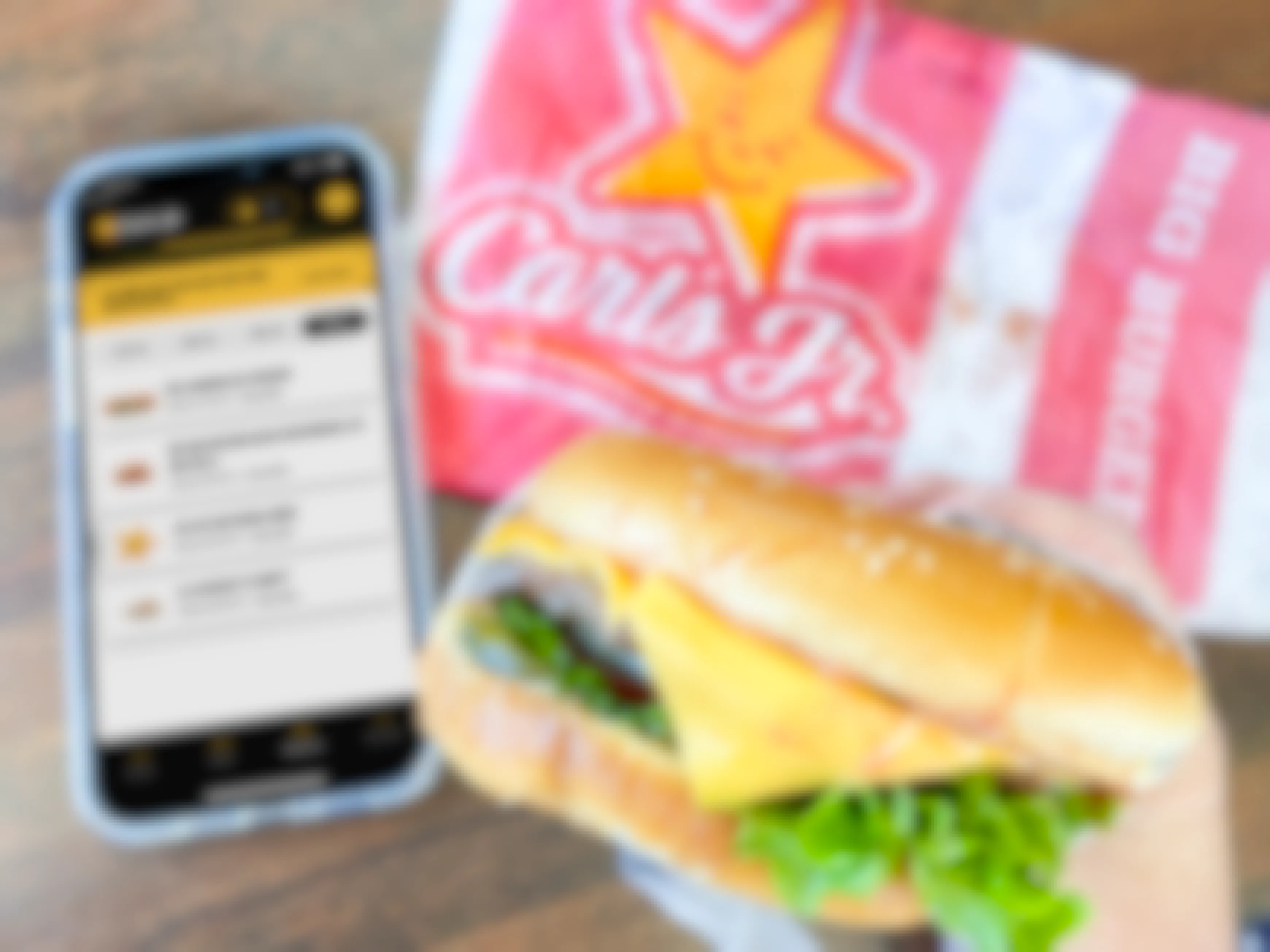 a person holding a cellphone with the carls jr app being held next to a carls jr burger