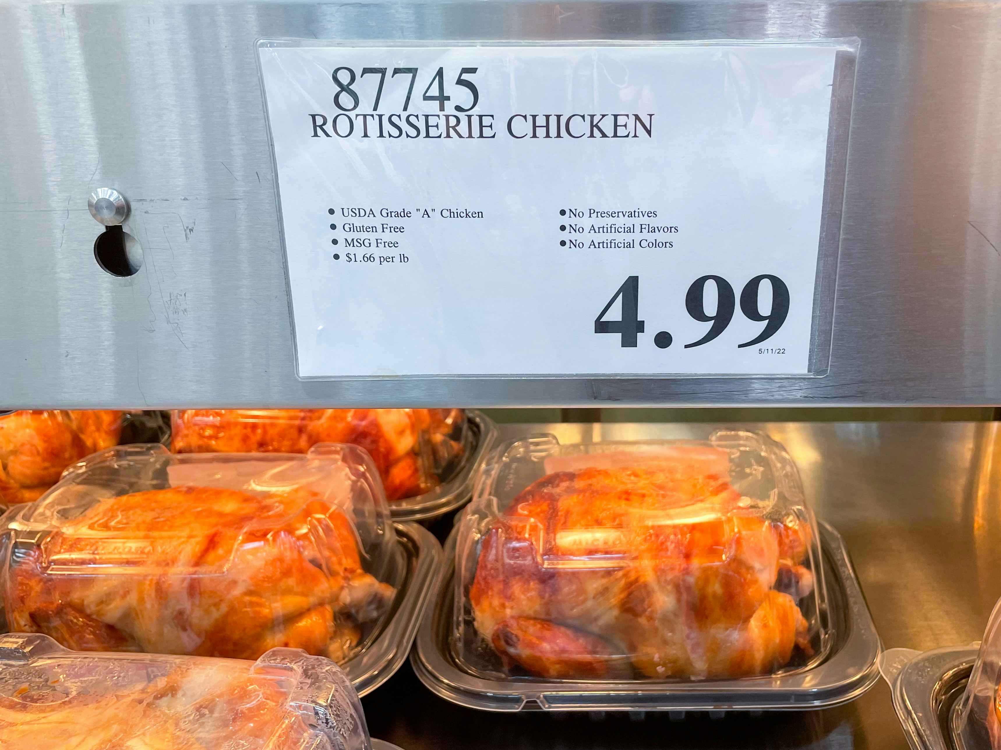 A hot shelf of boxed rotisserie chickens inside Costco with a price label of $4.99