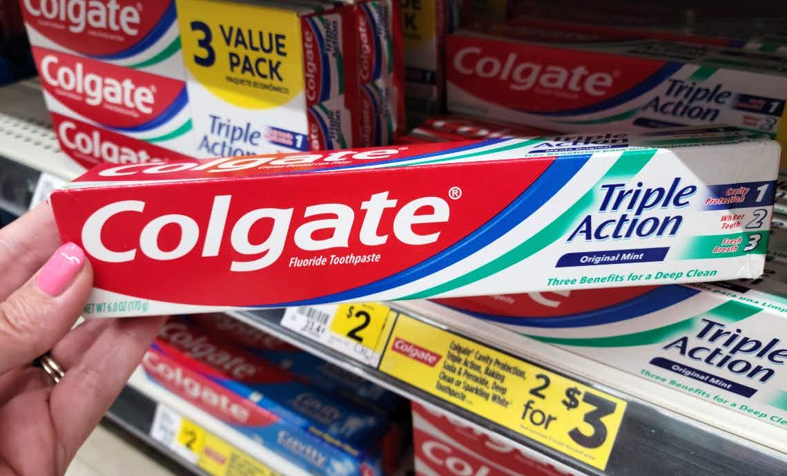 hand grabbing Colgate toothpaste off of store shelf